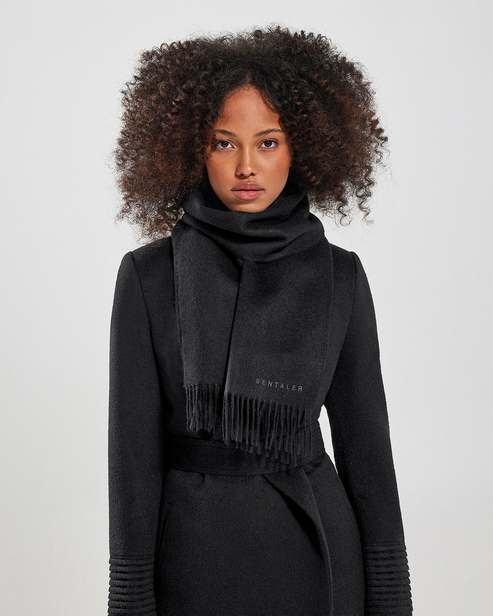 Front close up view of model wearing Sentaler's adult Black classic scarf, made of baby alpaca yarn. 