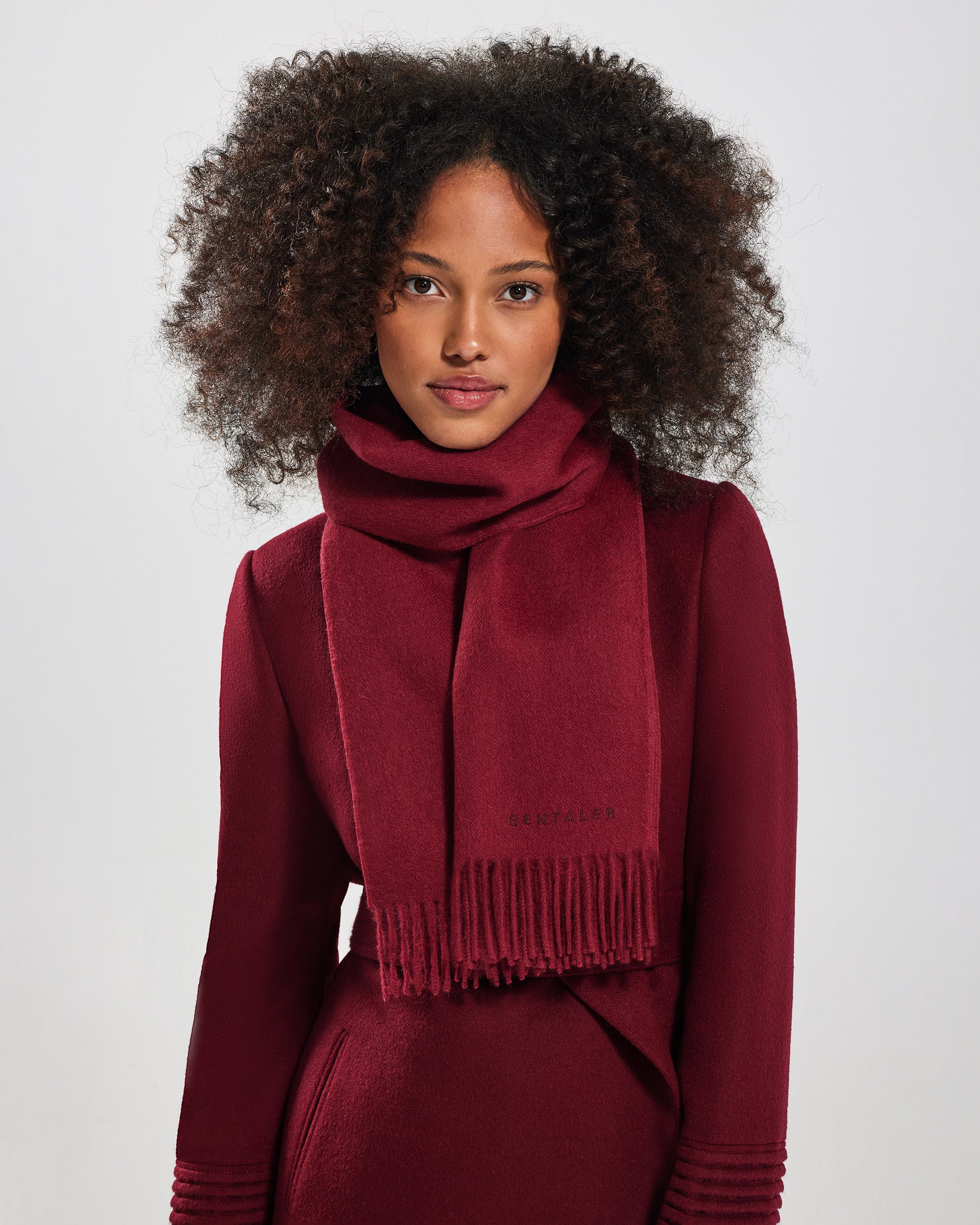 Direction view of model wearing Sentaler's adult Garnet Red classic scarf, made of baby alpaca yarn. 