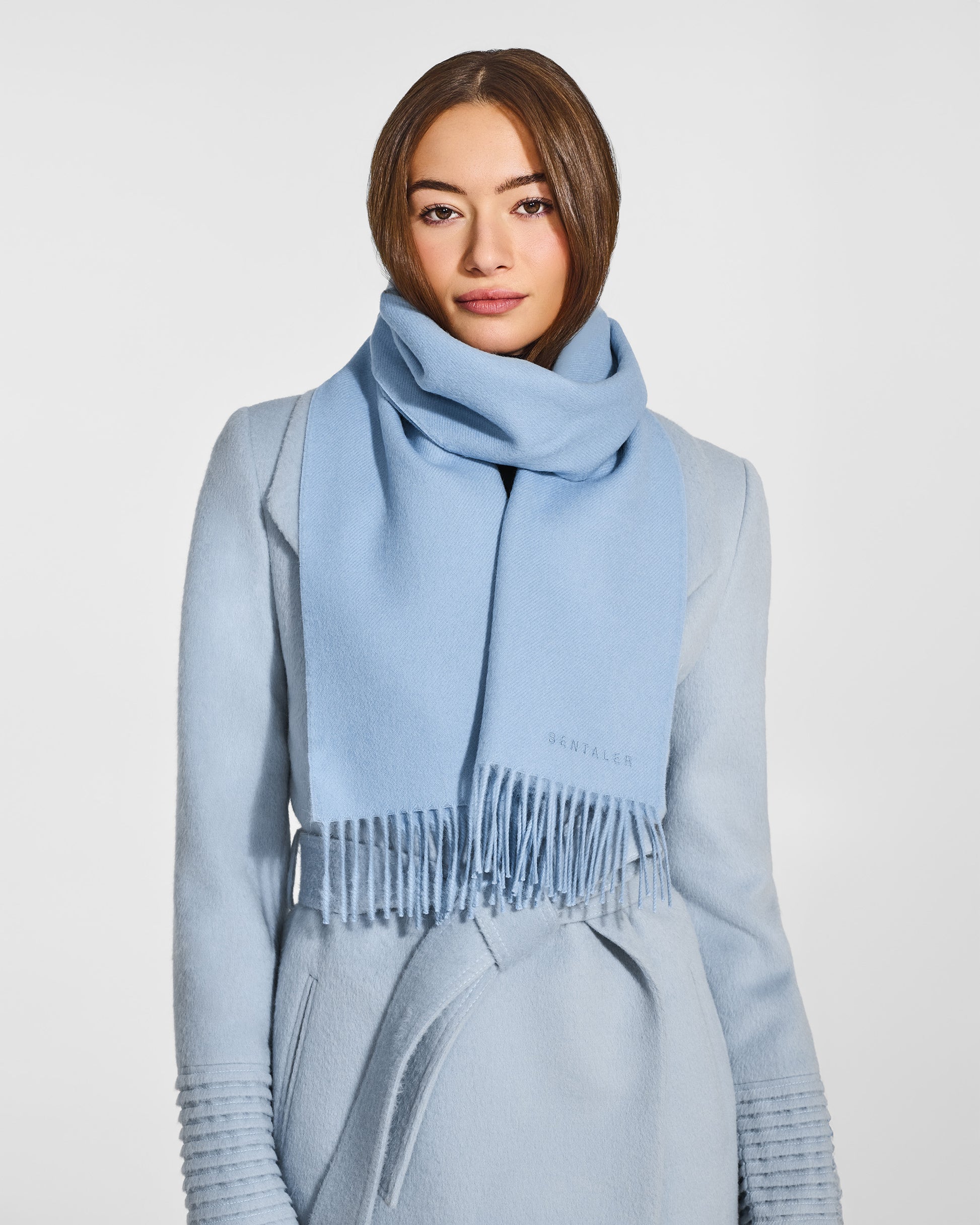 Front close up view of model wearing Sentaler's adult Powder Blue classic scarf, made of baby alpaca yarn. 