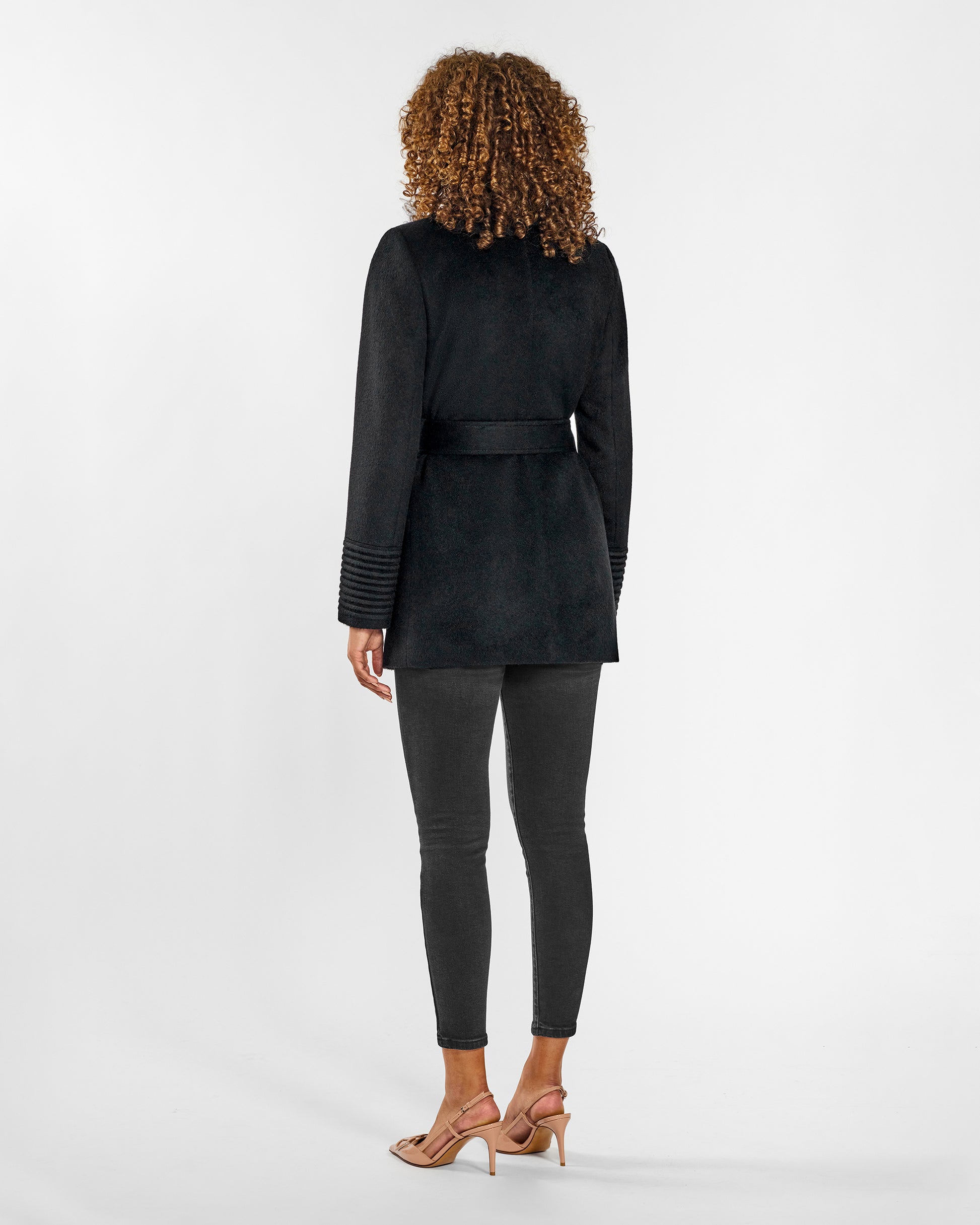 Back view of model wearing a SENTALER black cropped coat made of baby alpaca wool, with square pockets, worn belted.