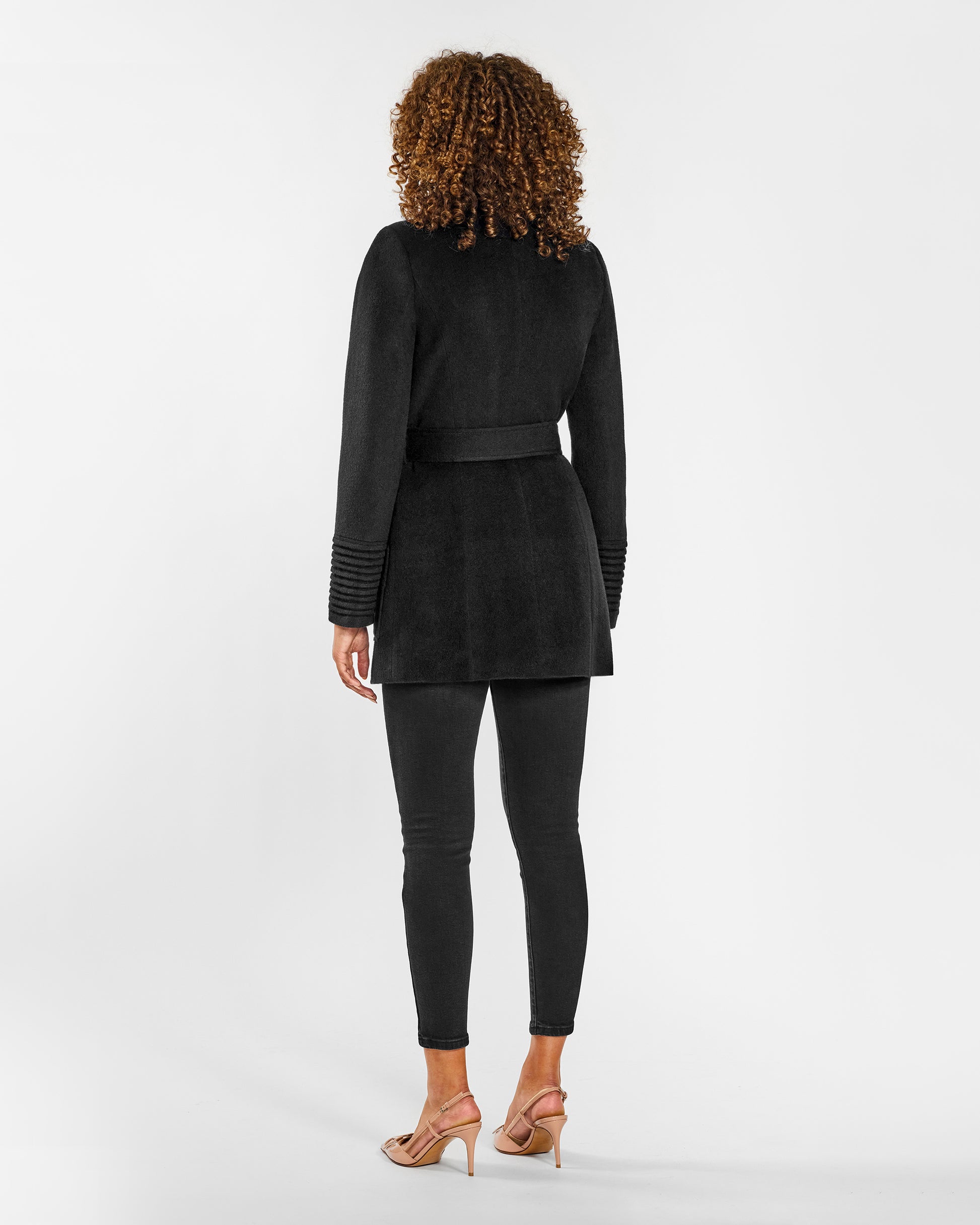 Back view of model wearing a Sentaler black cropped wrap coat made of baby alpaca wool, with a wide collar, worn belted.