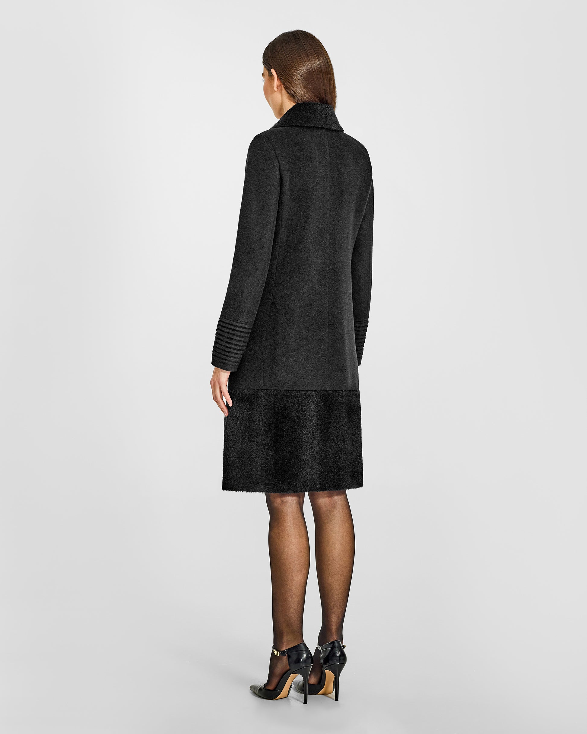 Back view of model wearing a Sentaler black A-line coat made of baby alpaca wool, with an empire waist, worn buttoned.