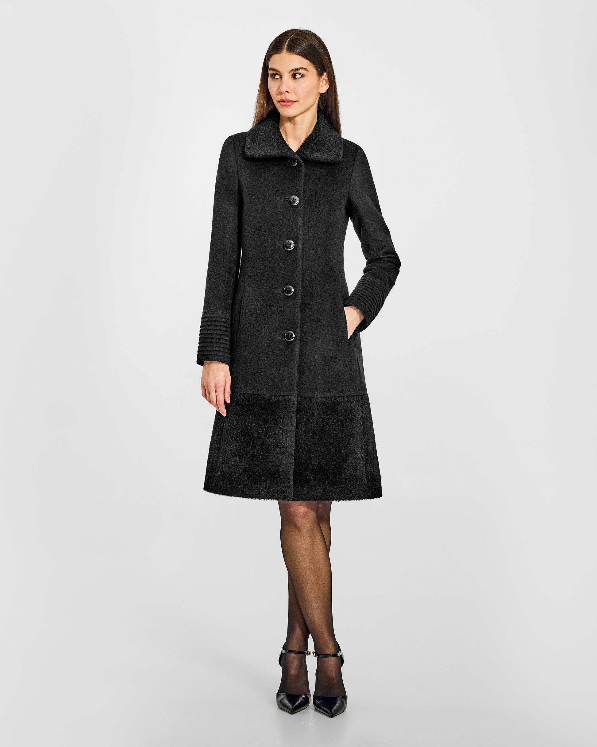 Front view of model wearing a Sentaler black A-line coat made of baby alpaca wool, with an empire waist, worn buttoned.