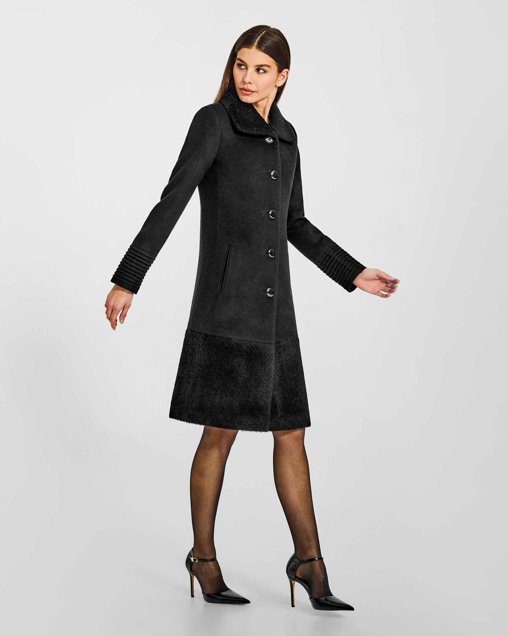 Side view of model wearing a Sentaler black A-line coat made of baby alpaca wool, with an empire waist, worn buttoned.