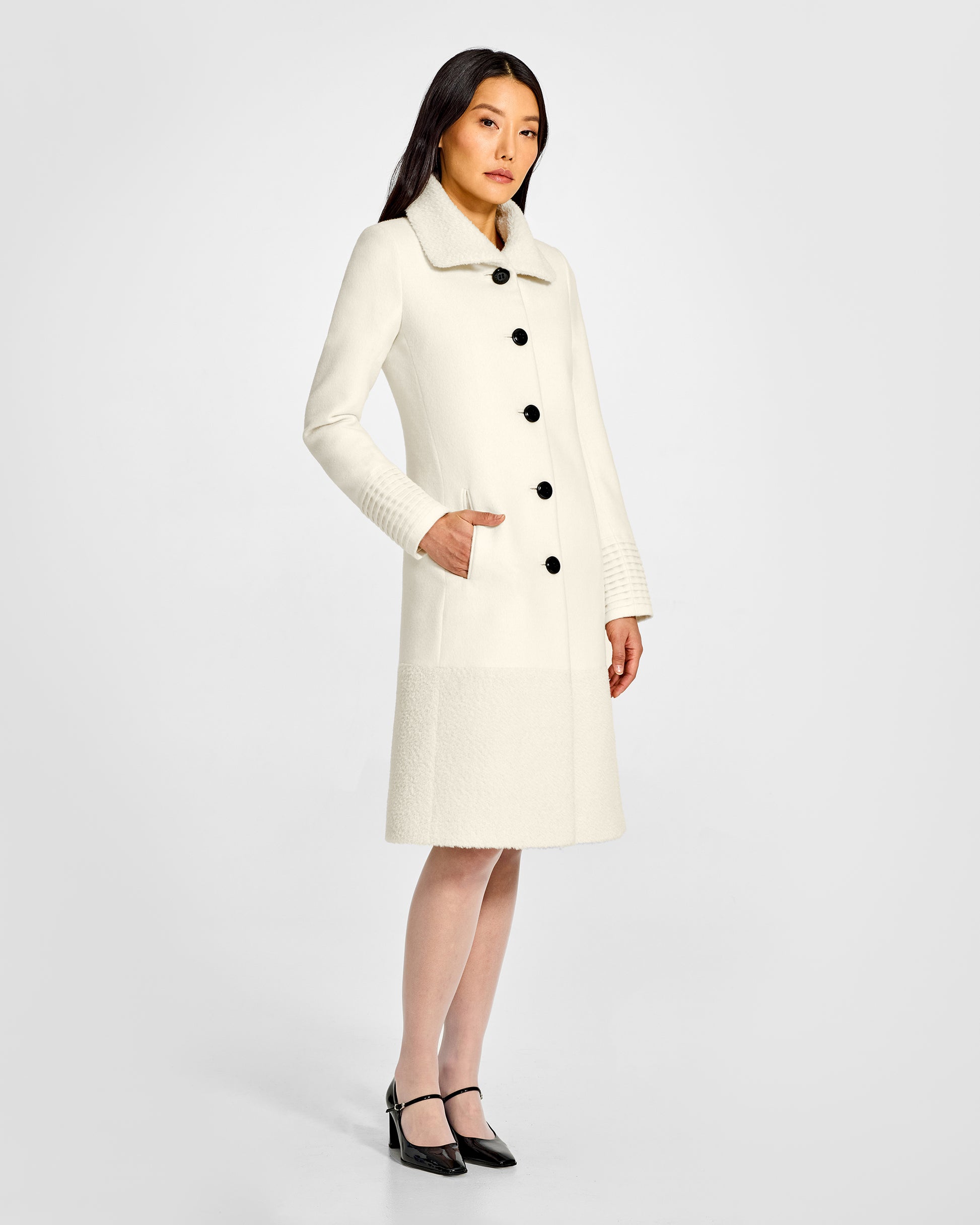 Side view of model wearing a Sentaler ivory A-line coat made of baby alpaca wool, with an empire waist, worn buttoned.