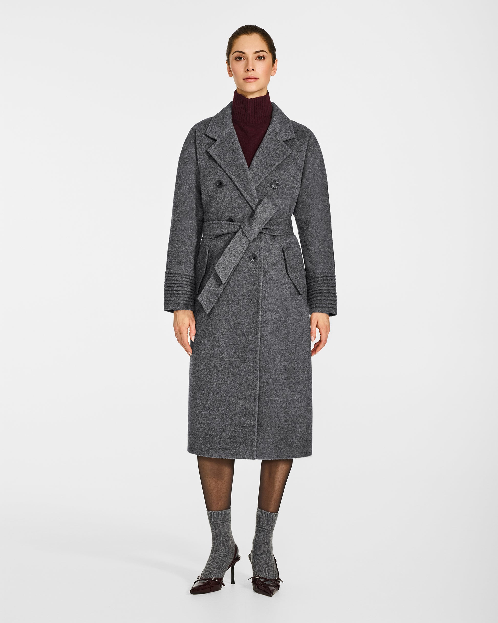 Front view of model wearing a Sentaler grey mélange double breasted coat made of baby alpaca wool, with a notched collar, worn belted.