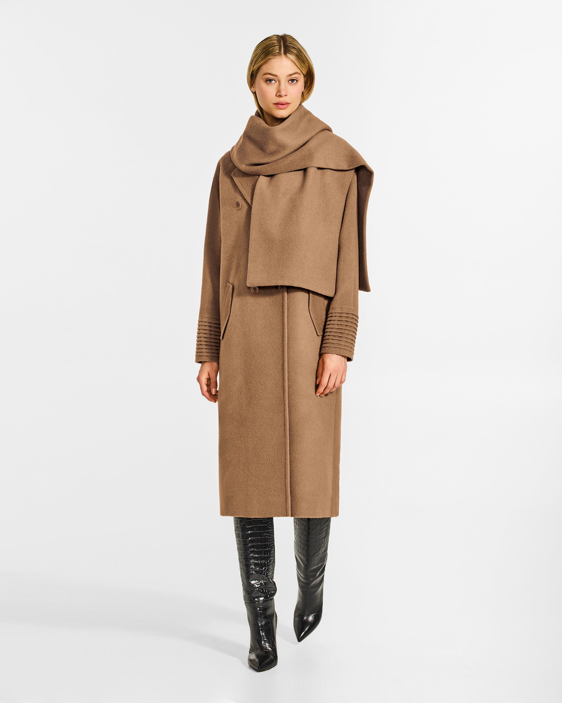 Front view of model wearing a Sentaler dark camel double breasted coat made of baby alpaca wool with a notched collar, worn with fabric scarf, buttoned.