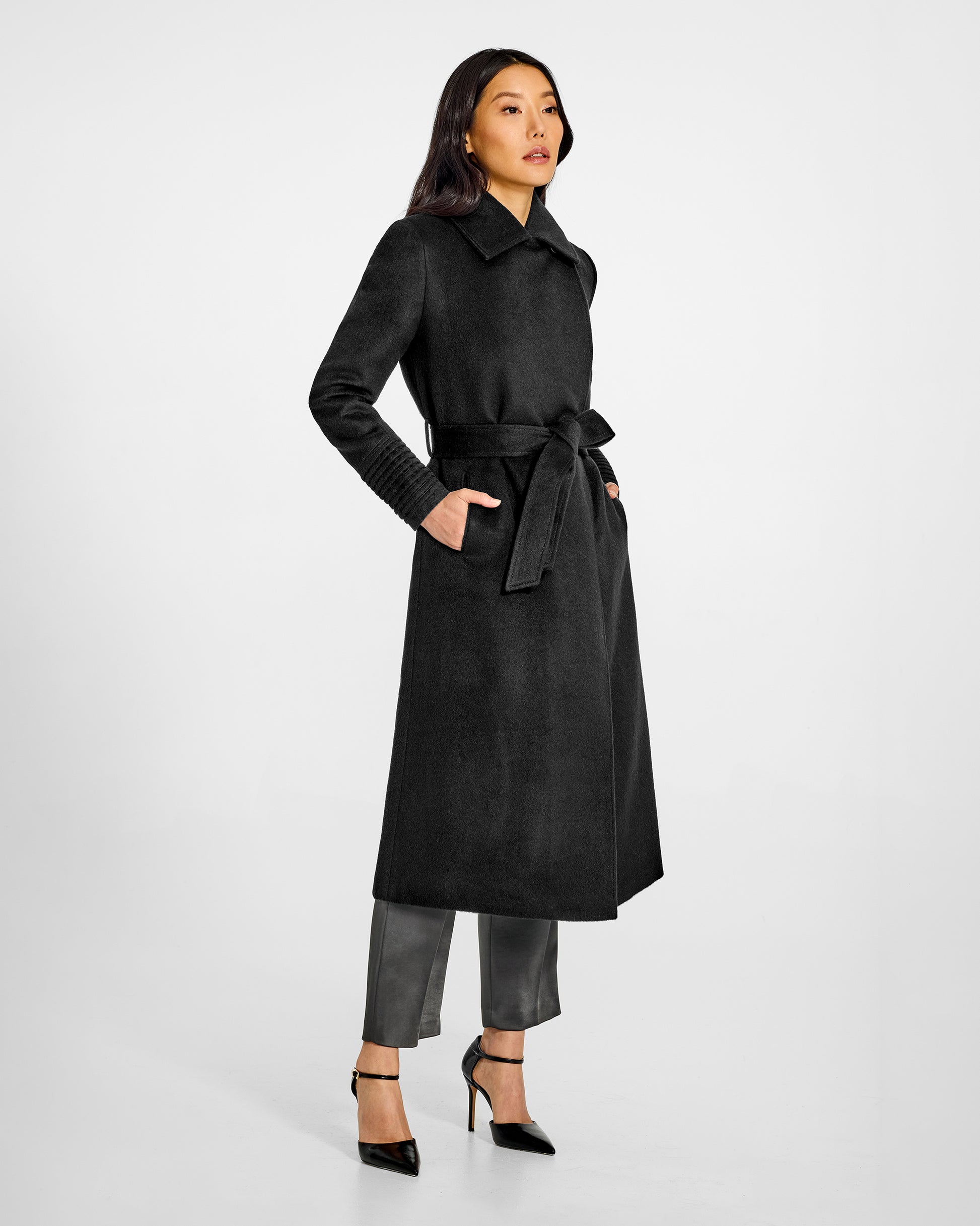 Side view of model wearing a Sentaler long black wrap coat made of baby alpaca wool, with a lapel collar, worn belted.