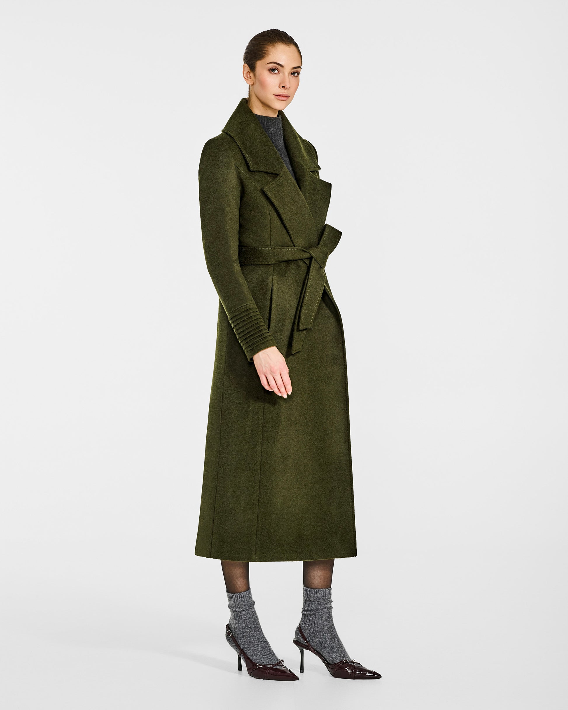 Side view of model wearing a SENTALER long olive green wrap coat made of baby alpaca wool, with a large notched collar, worn belted.