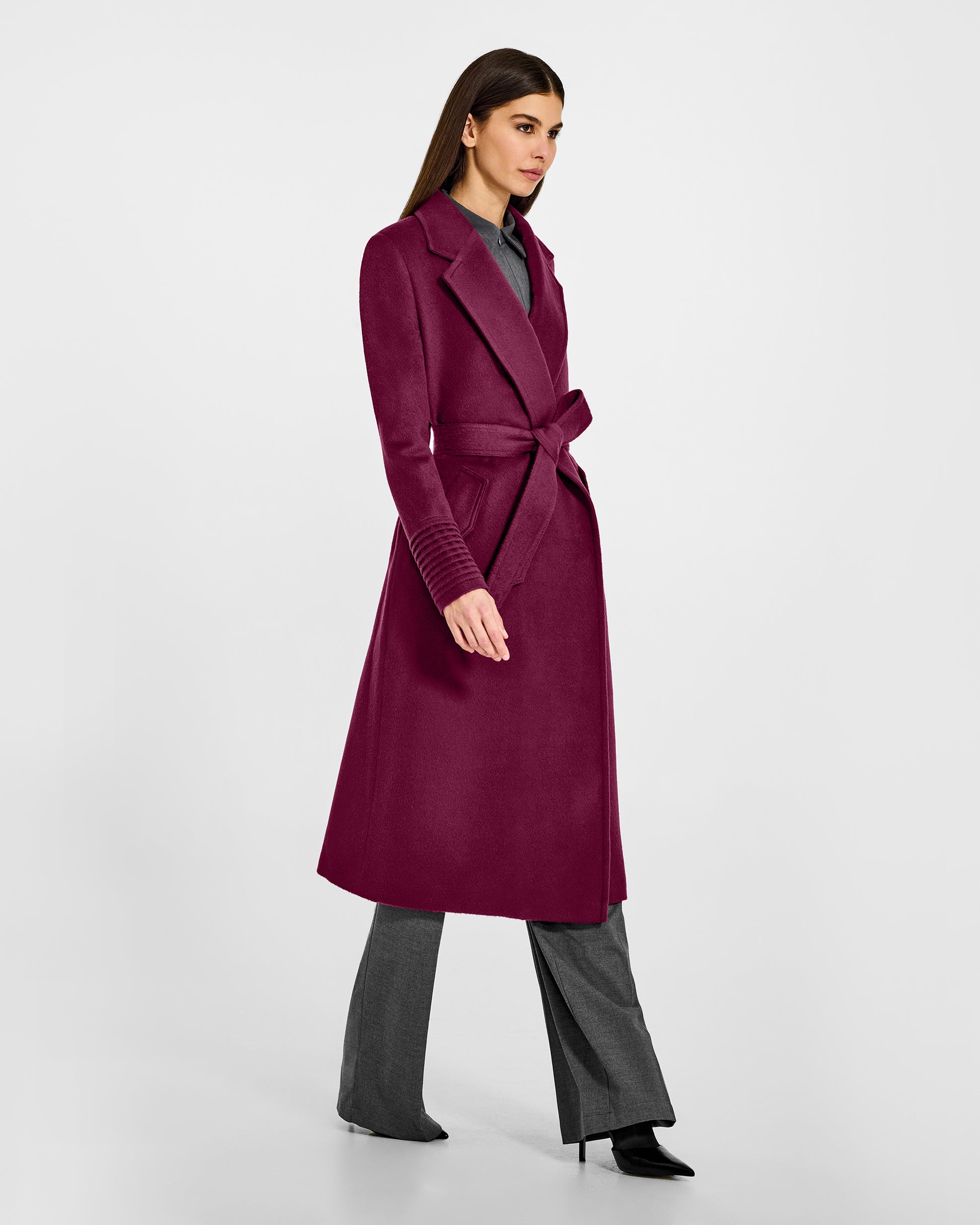 Side view of model wearing a Sentaler long plum berry purple wrap coat made of baby alpaca wool, with a notched collar, worn belted.