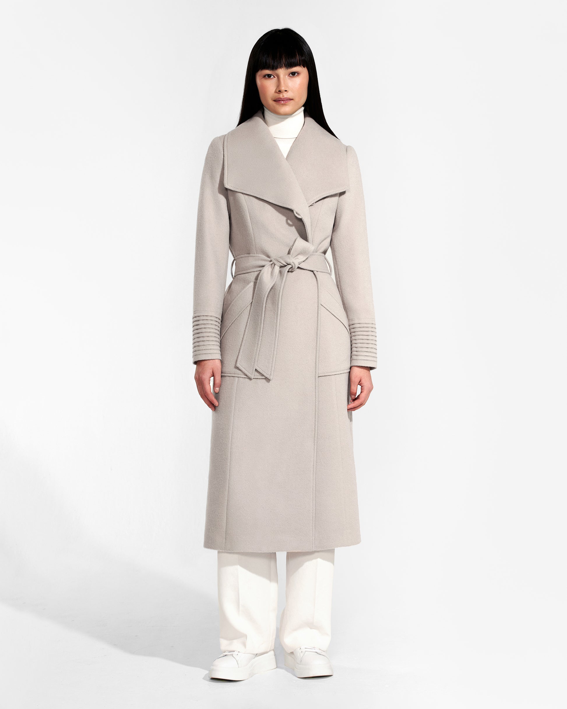 Front view of model wearing a Sentaler bleeker beige long wrap coat made of baby alpaca wool, with a wide collar, worn belted.