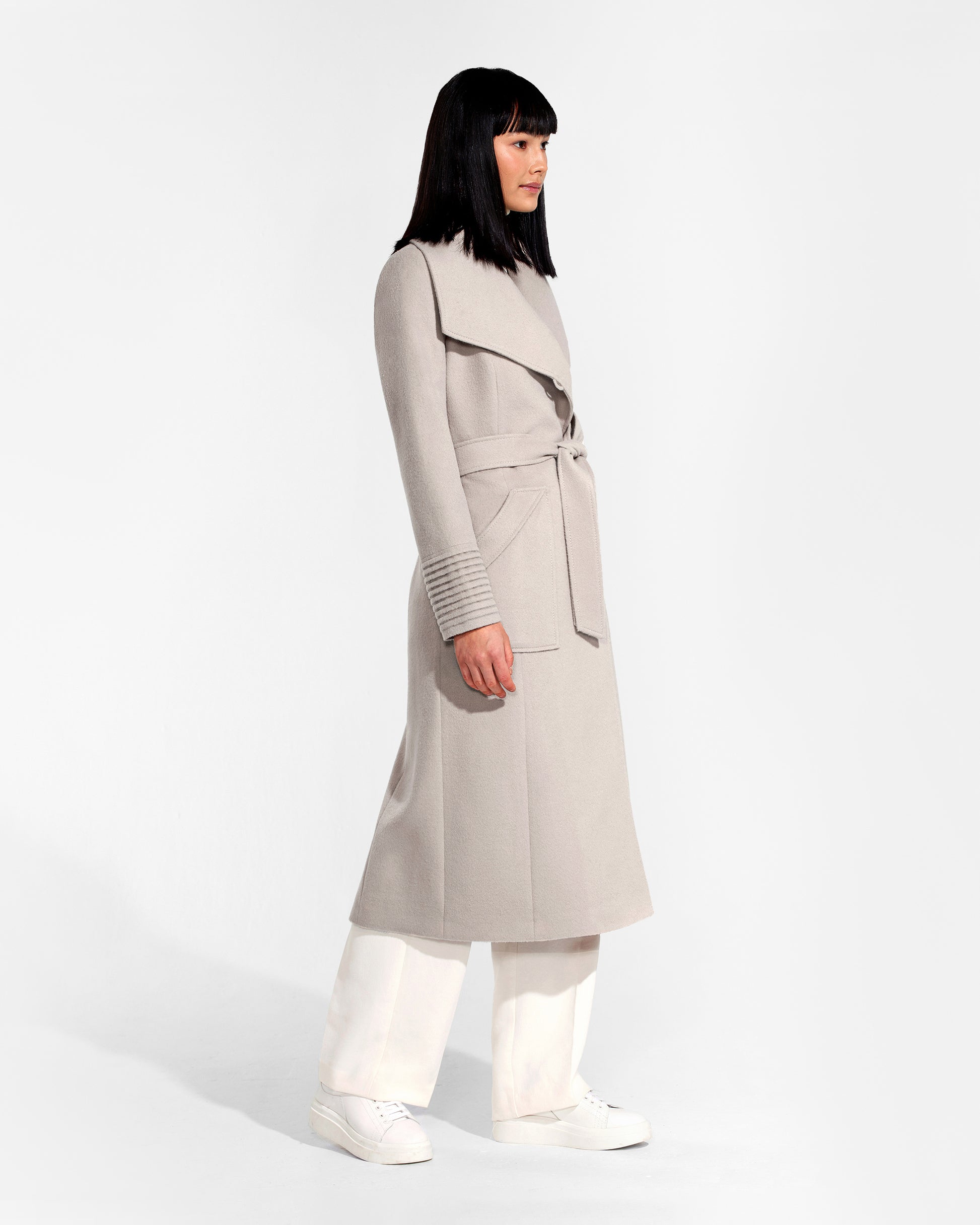 Side view of model wearing a Sentaler bleeker beige long wrap coat made of baby alpaca wool, with a wide collar, worn belted.