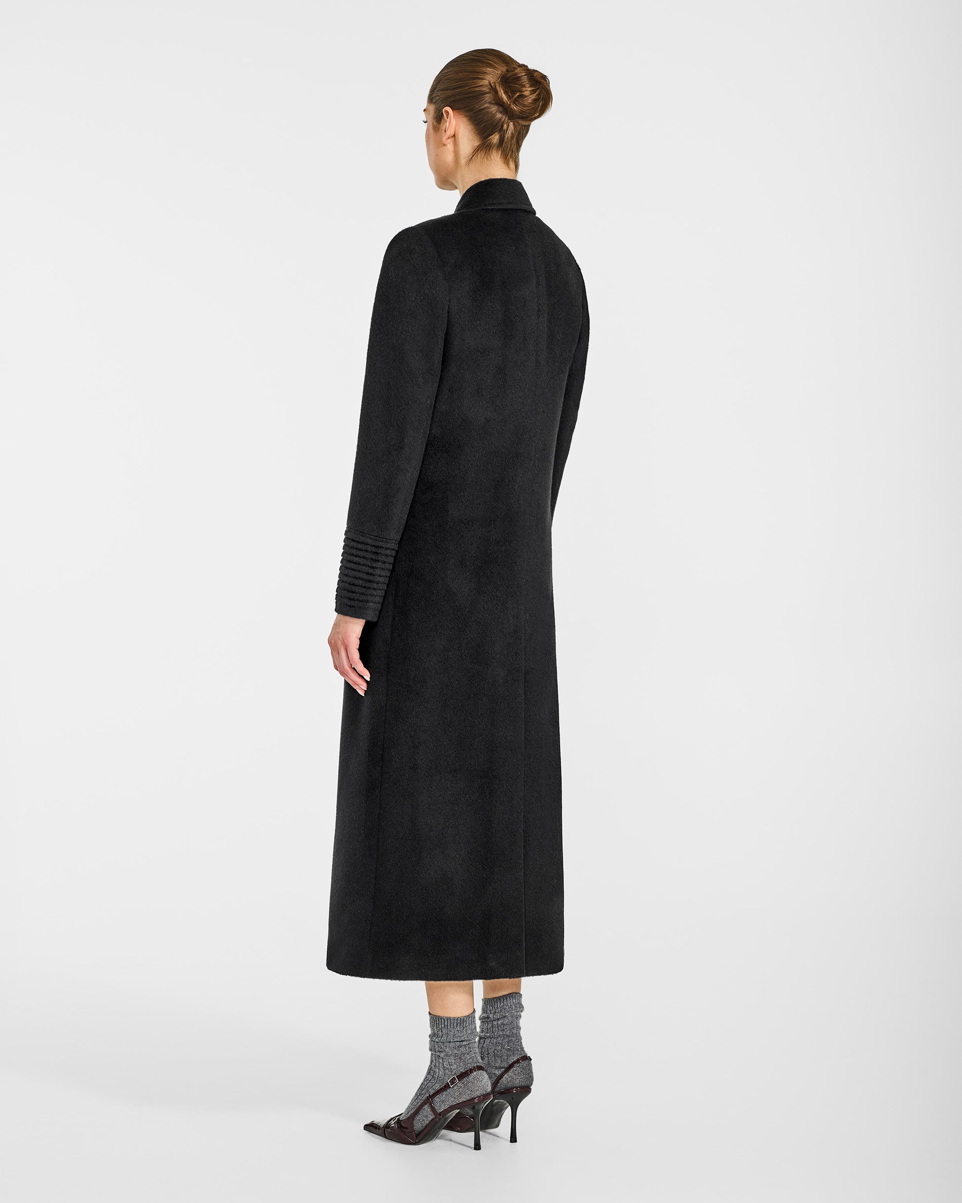 Back view of model wearing a Sentaler black double breasted maxi coat made of baby alpaca wool, with a peak collar, worn buttoned.