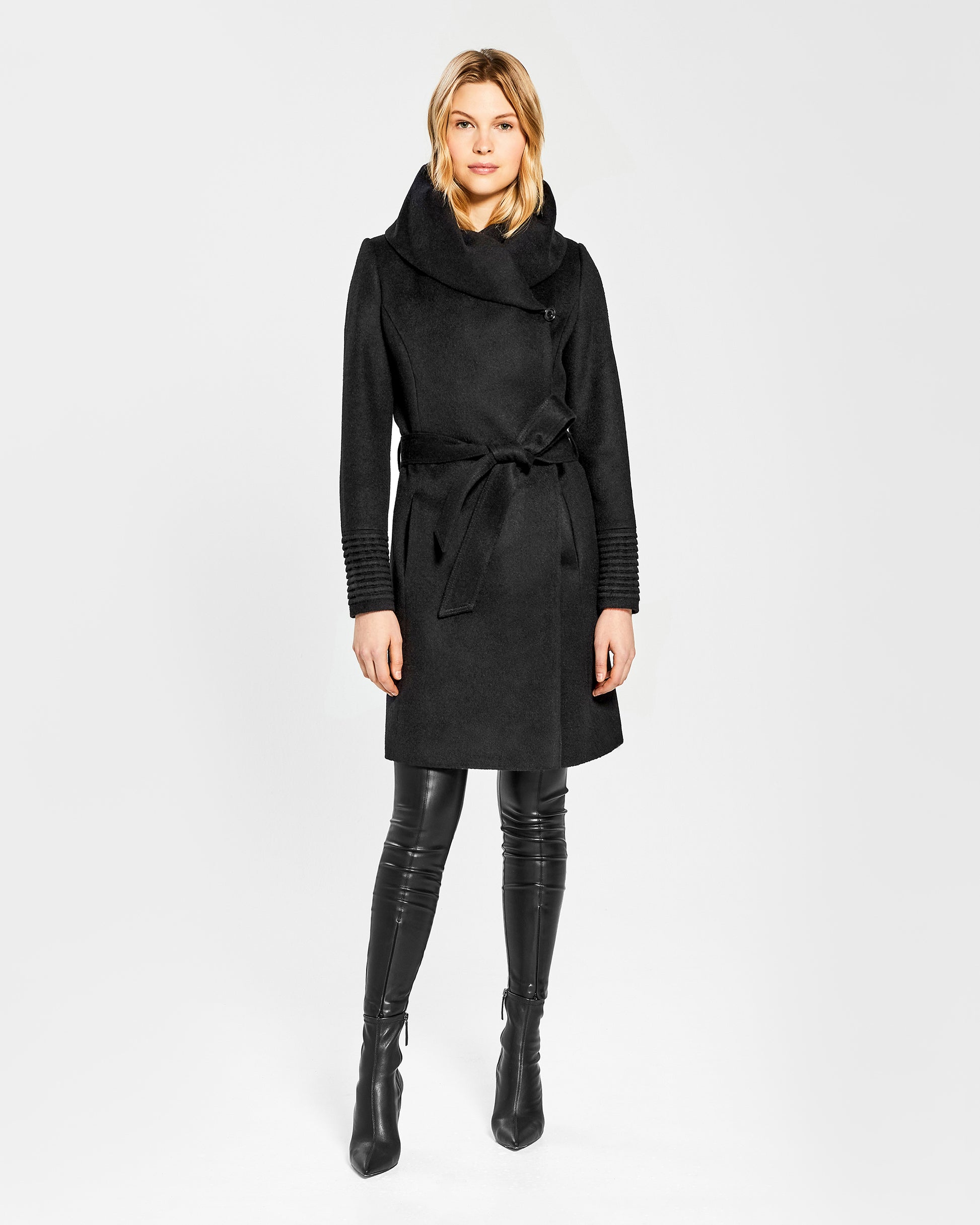Front view of model wearing a Sentaler mid length black coat made of baby alpaca wool, with a hooded collar, worn belted.