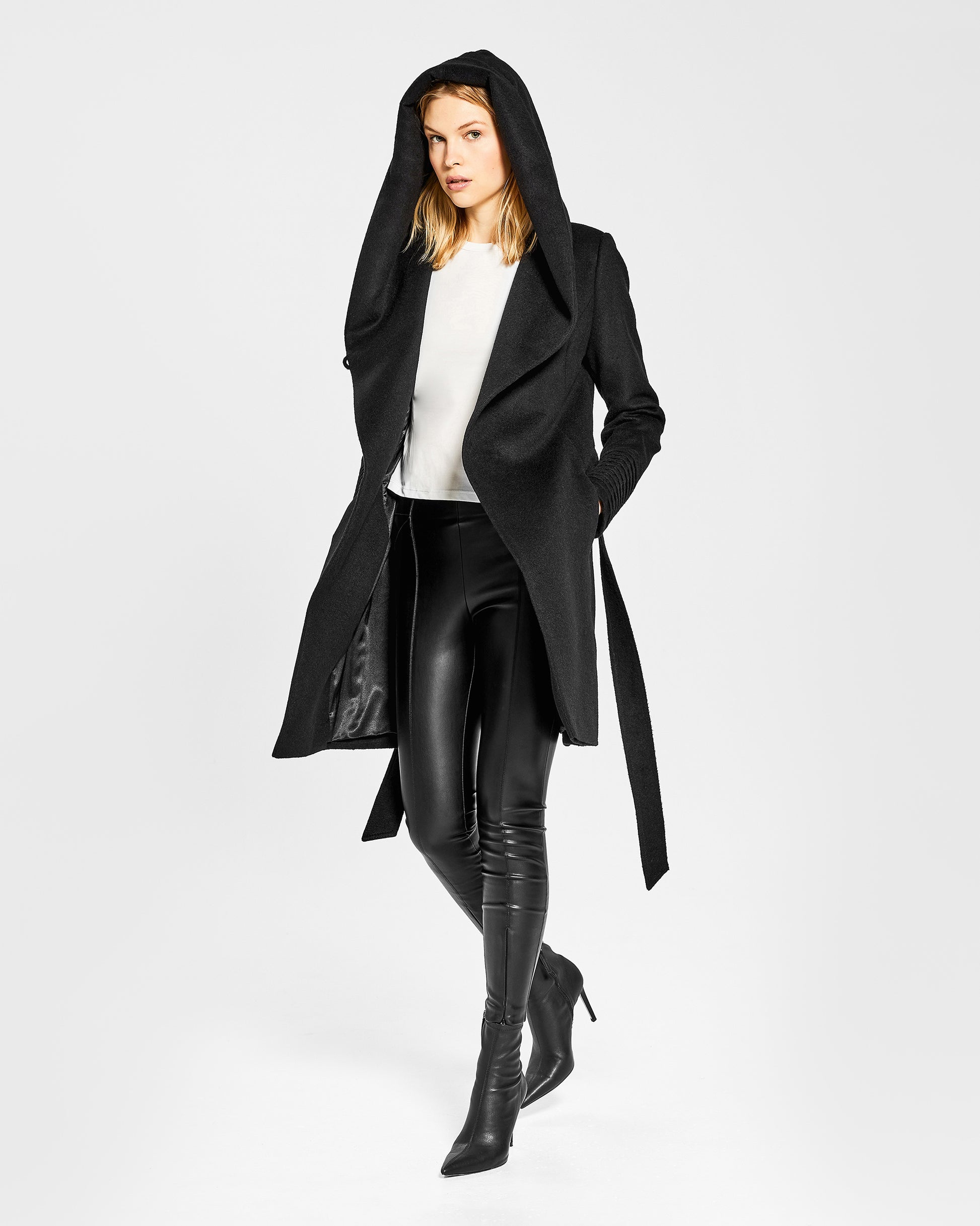 Side view of model wearing a Sentaler mid length black coat made of baby alpaca wool, with a hooded collar, worn hooded.
