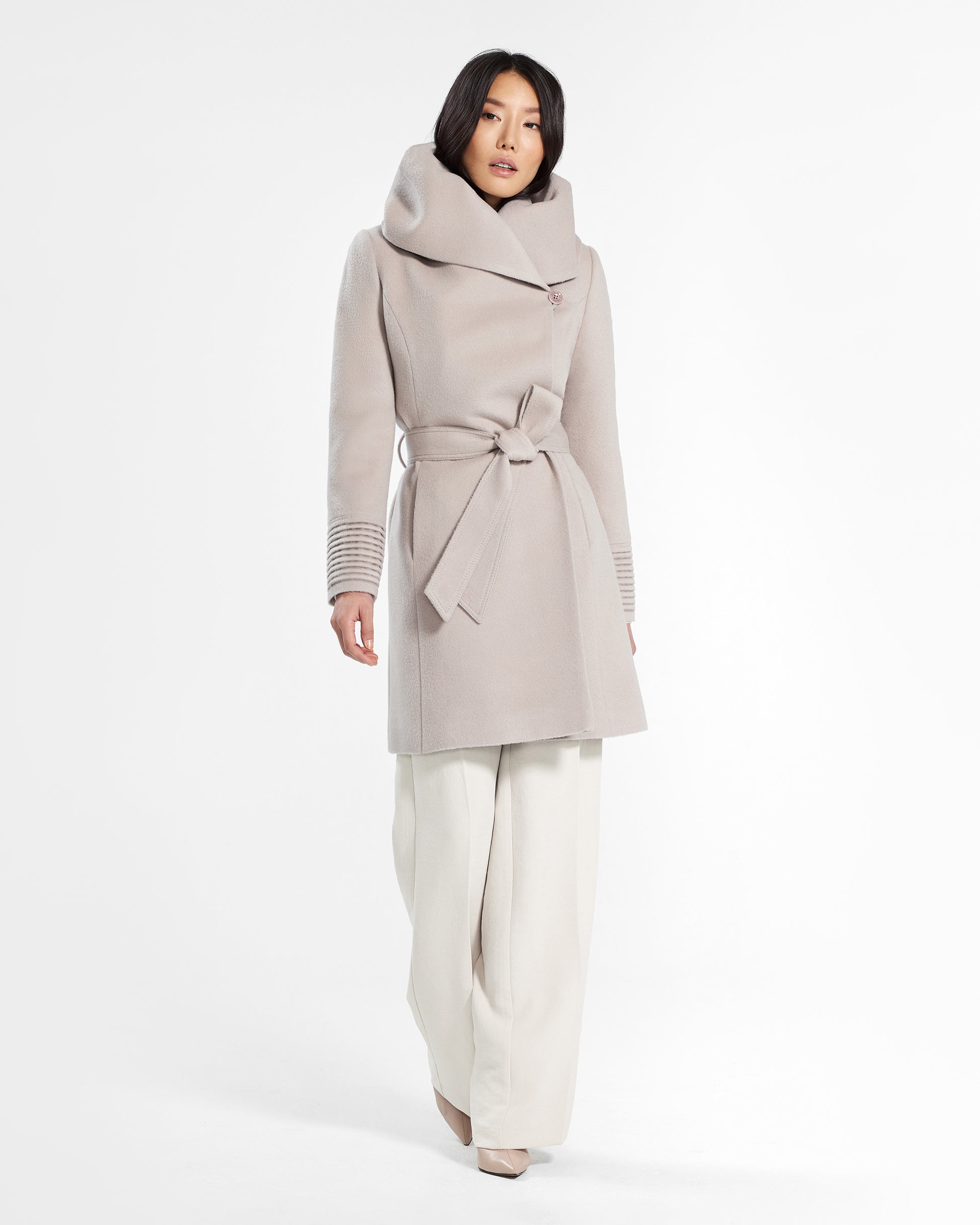 Front view of model wearing a Sentaler mid length bleeker beige coat made of baby alpaca wool, with a hooded collar, worn belted.