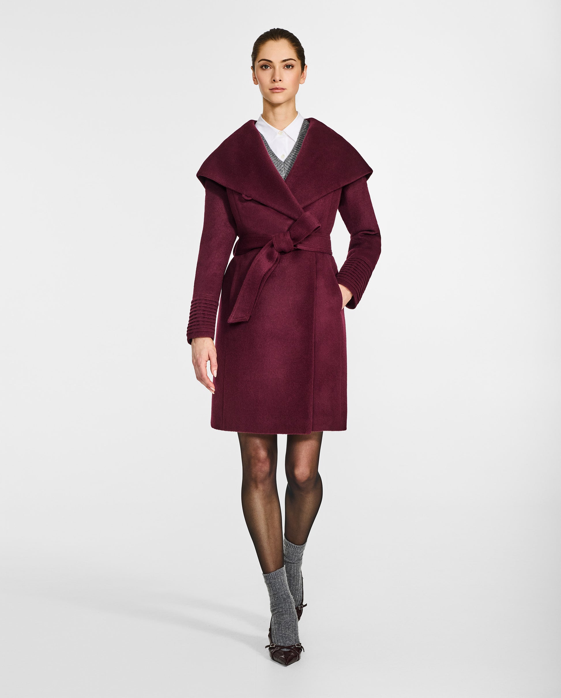 Front view of model wearing a Sentaler mid length cherry lacquer coat made of baby alpaca wool, with a hooded collar, worn belted with shawl collar.
