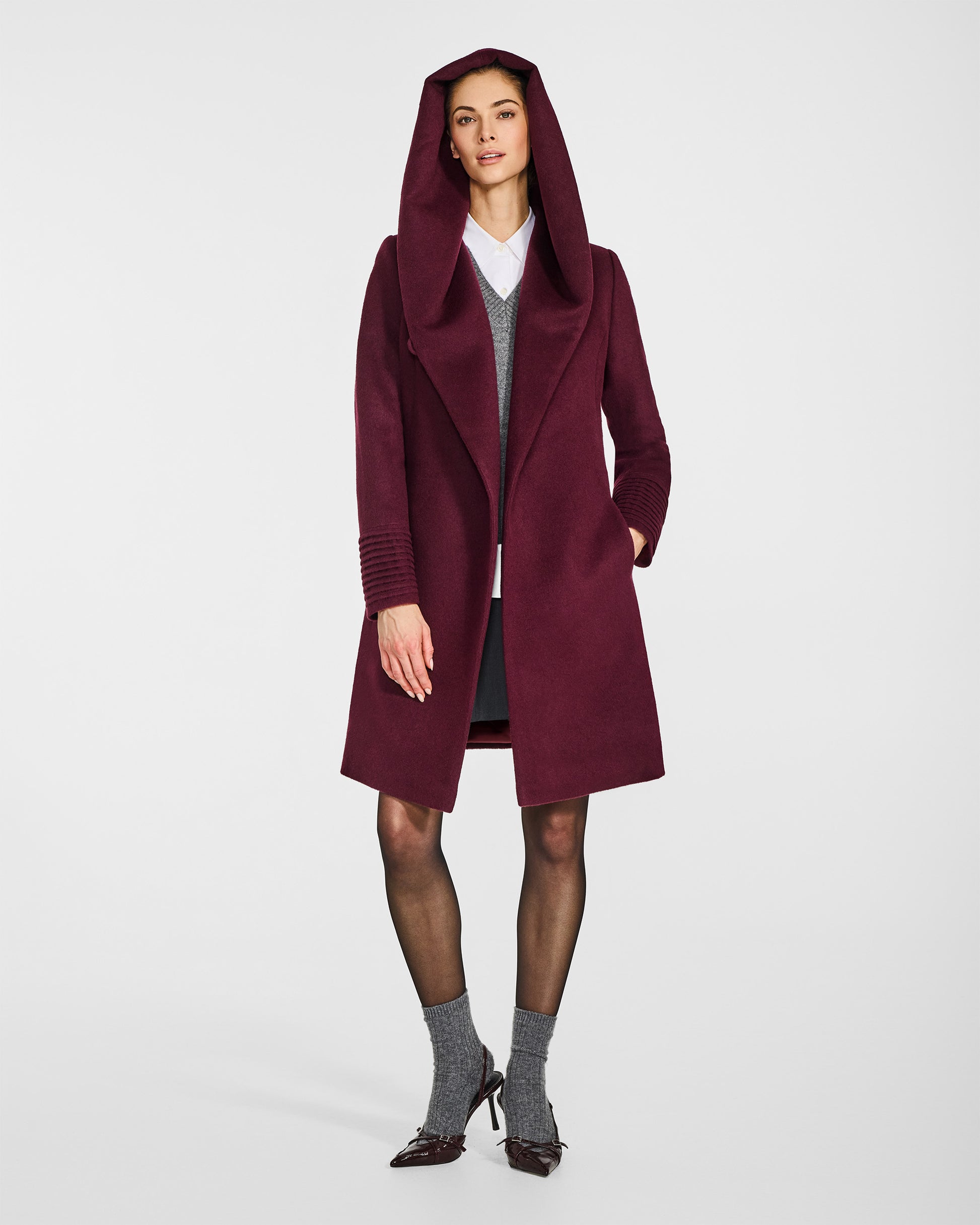 Front view of model wearing a Sentaler mid length cherry lacquer coat made of baby alpaca wool, with a hooded collar, worn open.