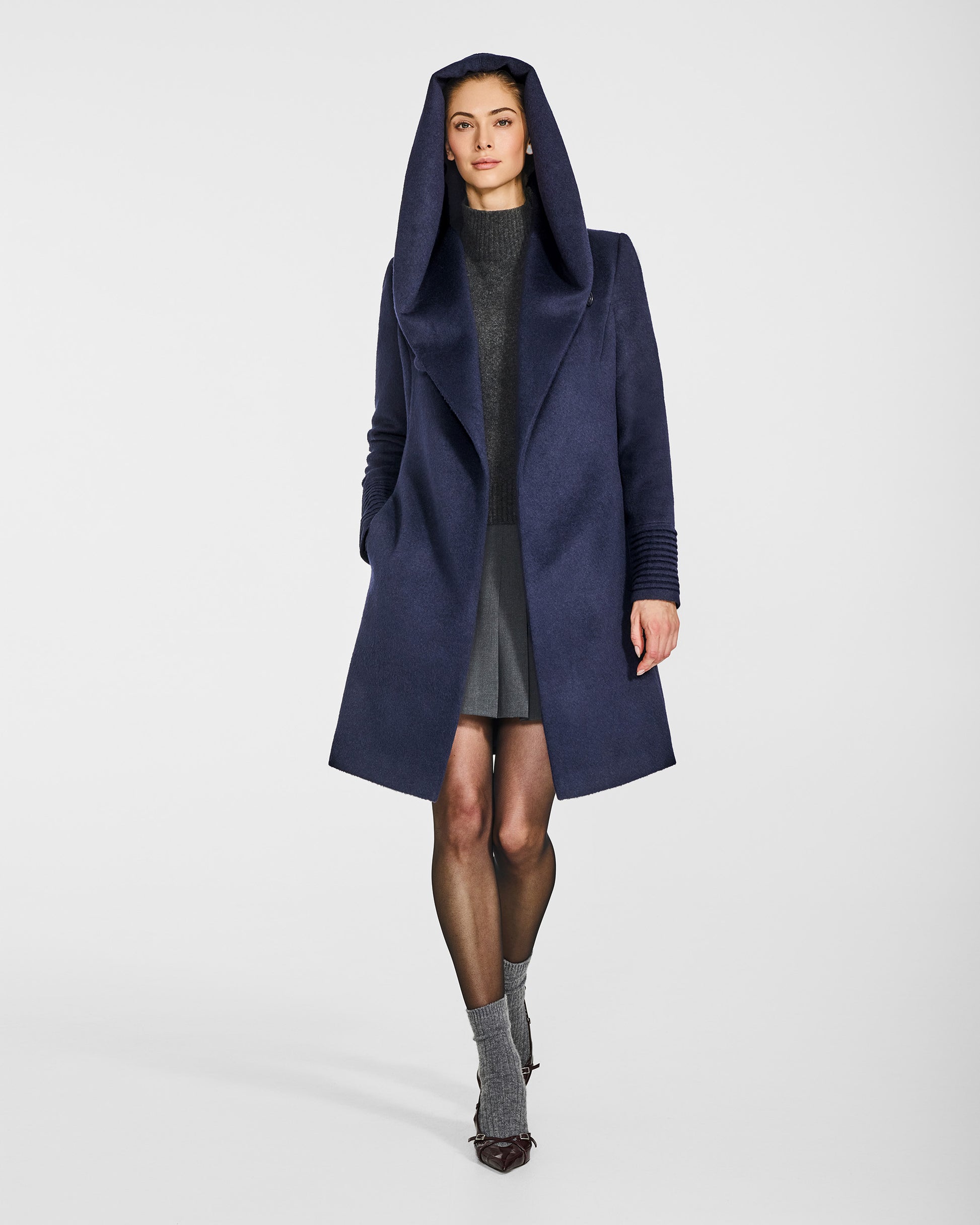 Front view of model wearing a Sentaler mid length deep navy coat made of baby alpaca wool, with a hooded collar, worn open.