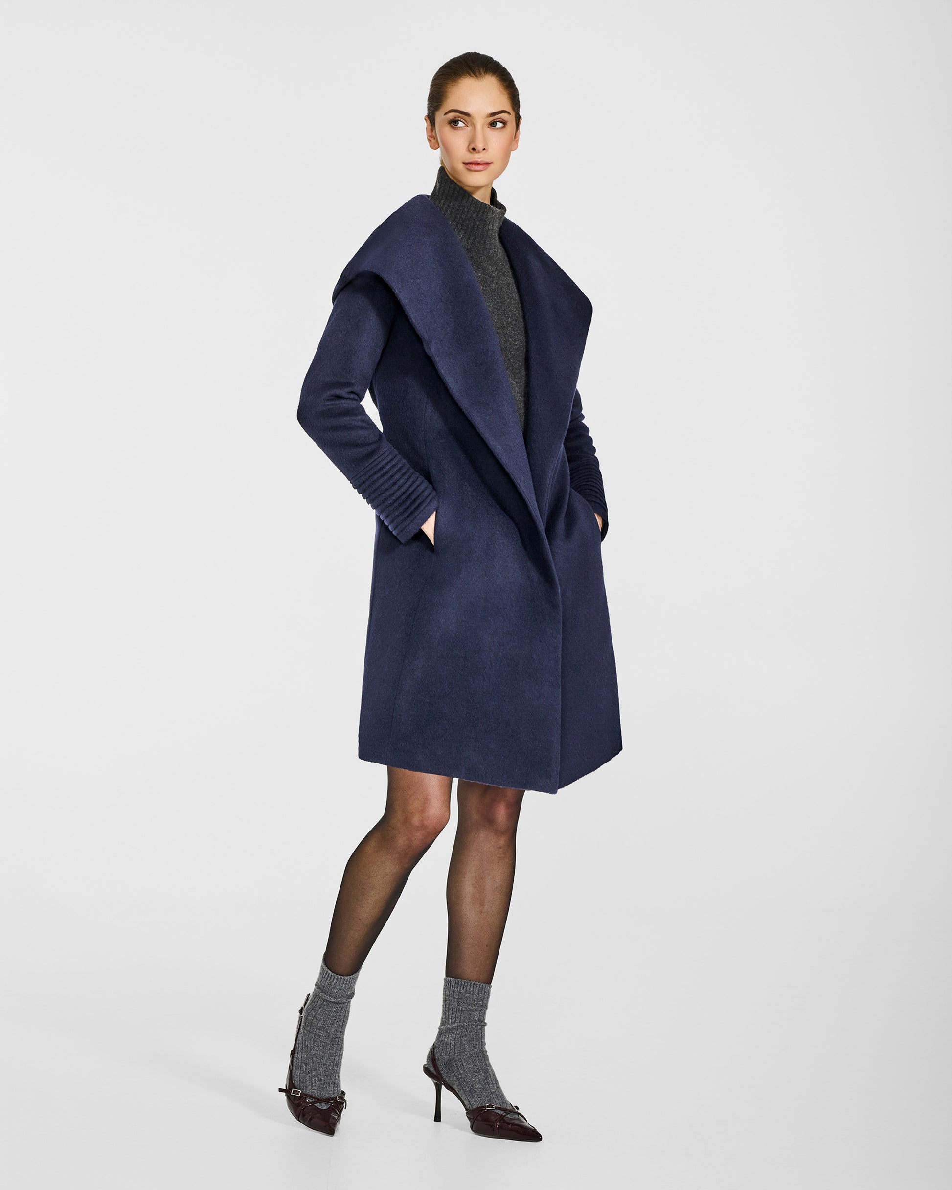 Side view of model wearing a Sentaler mid length deep navy coat made of baby alpaca wool, with a hooded collar, worn open.