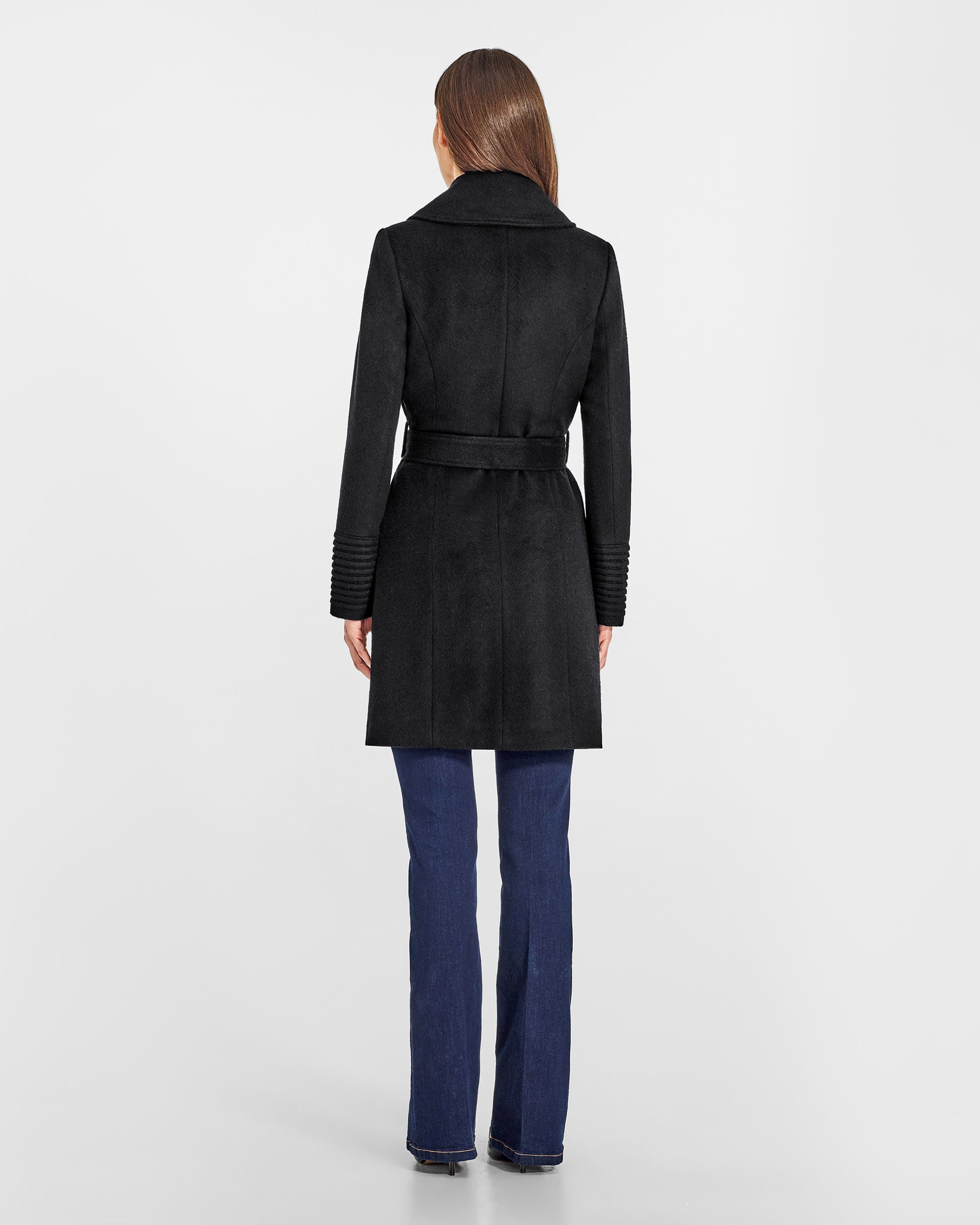 Back view of model wearing a Sentaler mid length black coat made of baby alpaca wool, with a large notched collar, worn belted.