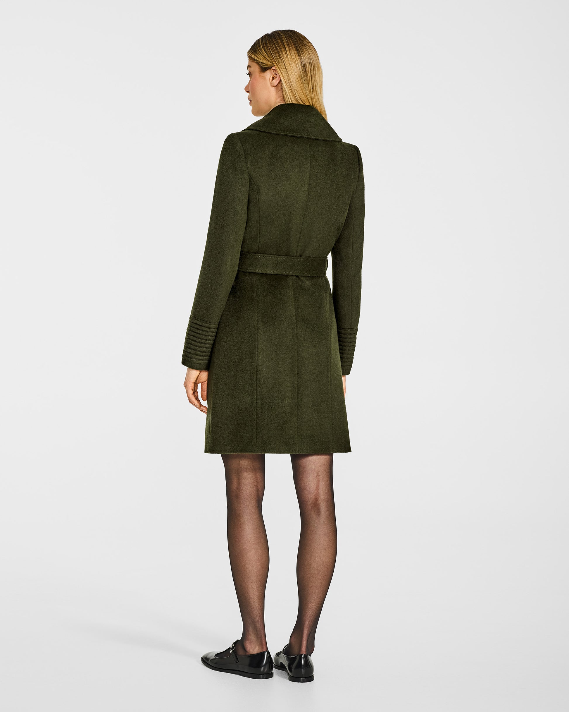 Back view of model in Sentaler mid length olive green coat with large notched collar in baby alpaca wool, belted.