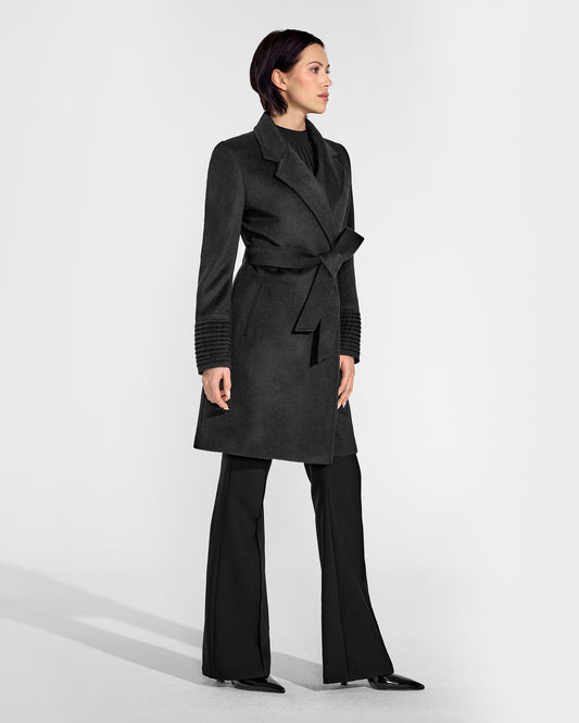 Side view of model wearing a Sentaler mid length black coat made of baby alpaca wool, with a notched collar, worn belted.