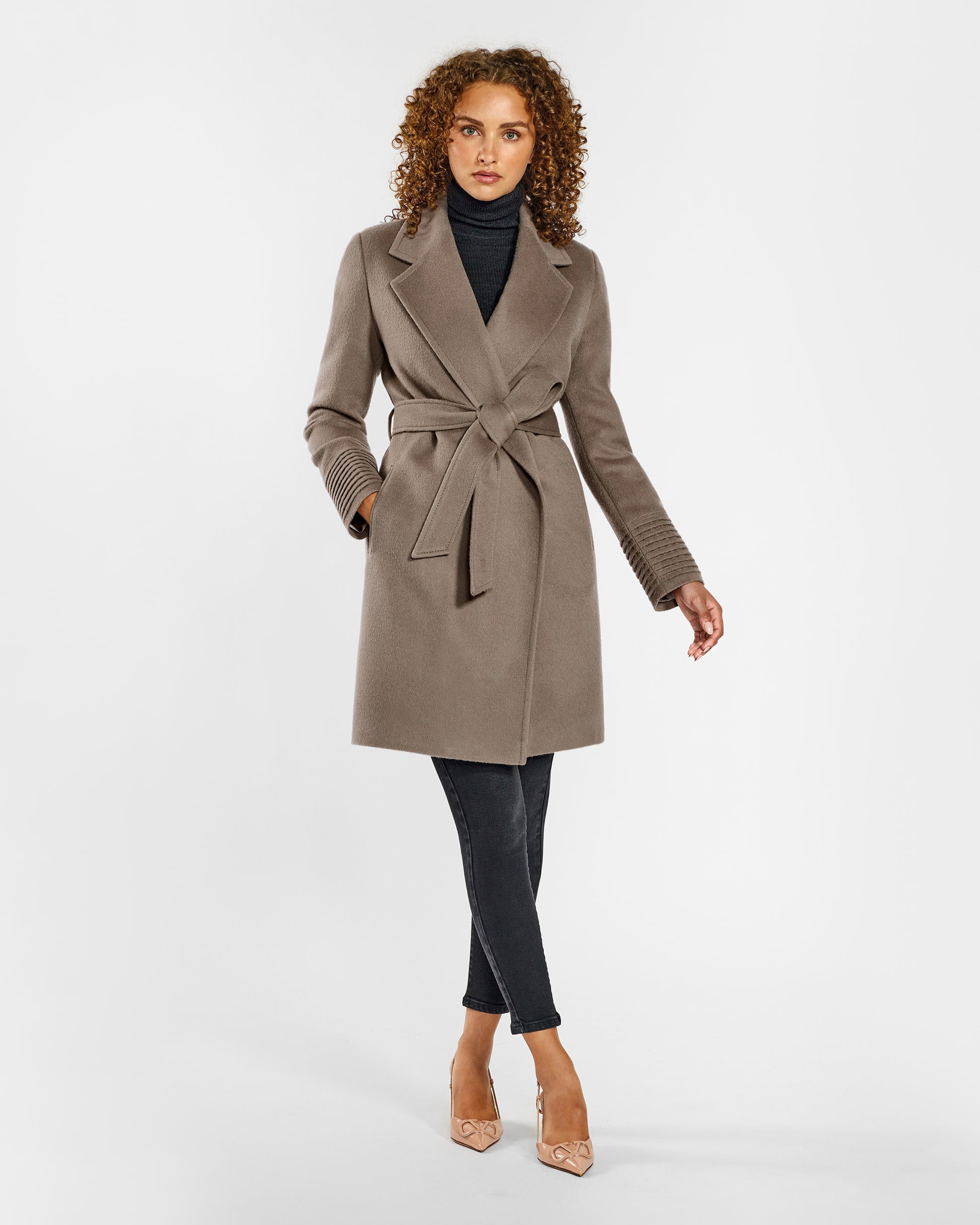 Front view of model wearing a Sentaler mid length warm taupe coat made of baby alpaca wool, with a notched collar, worn belted.