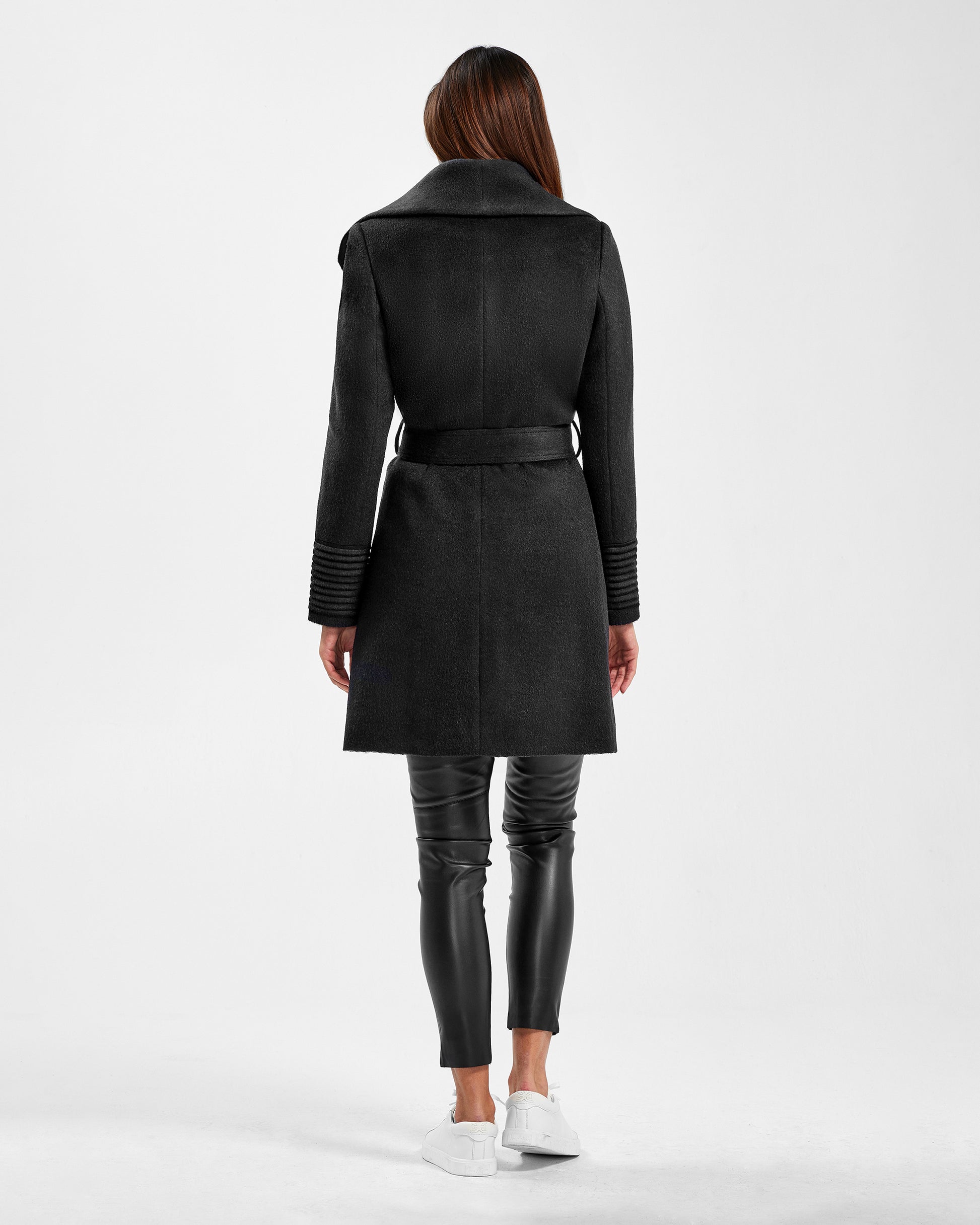 Back view of model wearing a Sentaler mid length black coat made of baby alpaca wool, with a shawl collar, worn belted.
