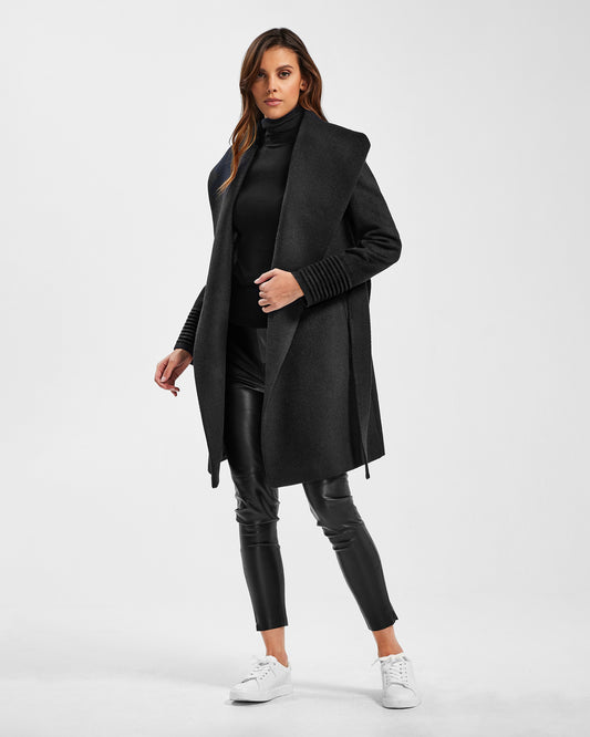 Front view of model wearing a Sentaler mid length black coat made of baby alpaca wool, with a shawl collar, worn open.