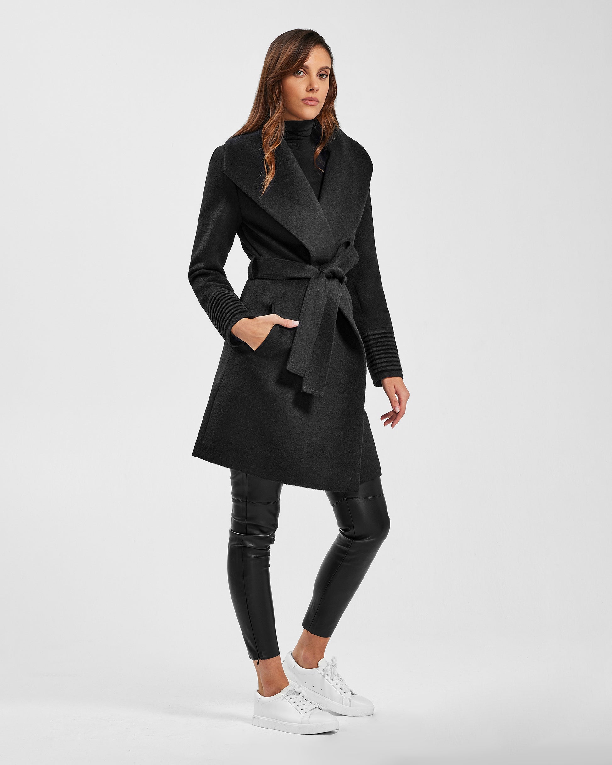 Side view of model wearing a Sentaler mid length black coat made of baby alpaca wool, with a shawl collar, worn belted.