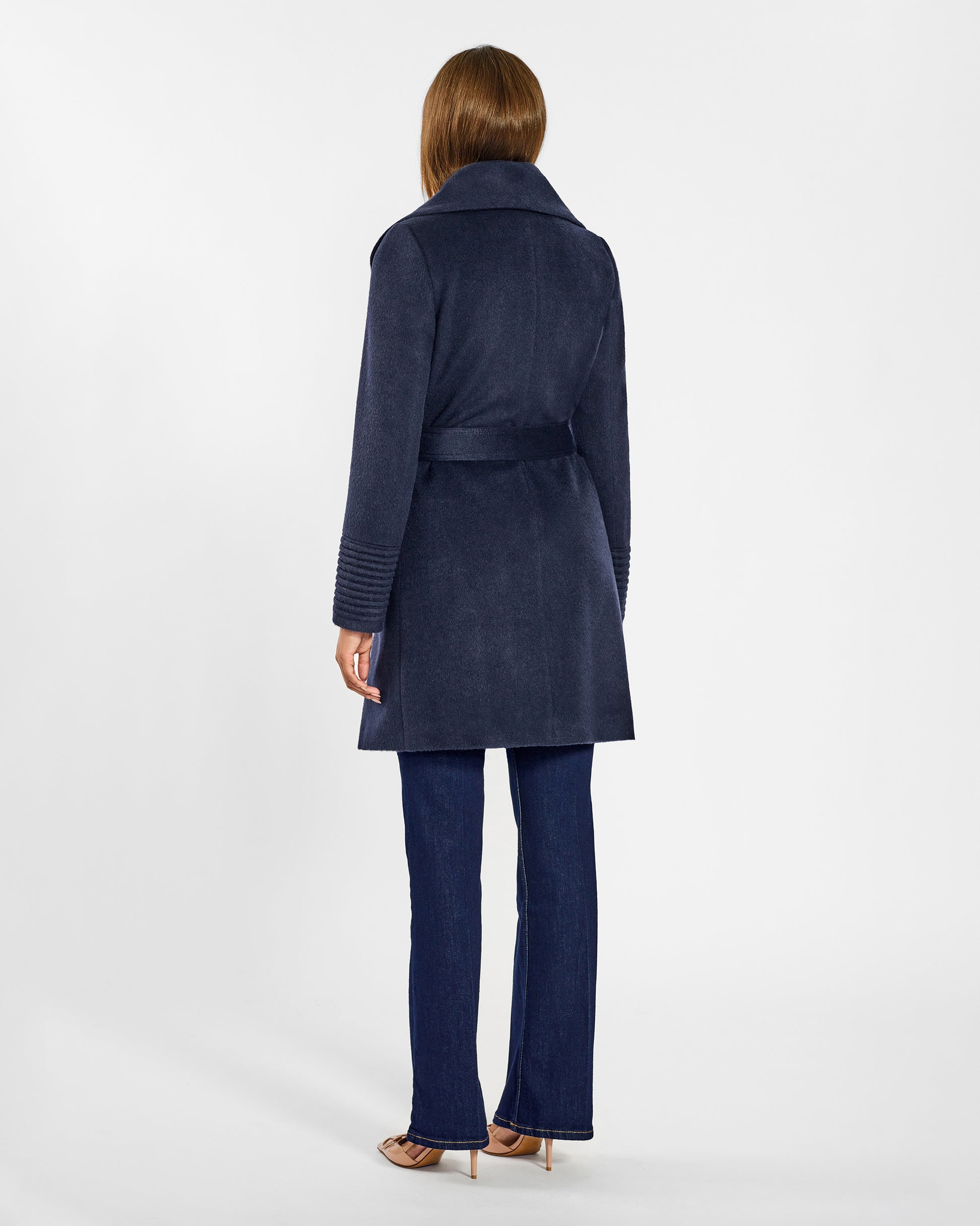 Back view of model wearing a Sentaler mid length deep navy coat made of baby alpaca wool, with a shawl collar, worn belted.