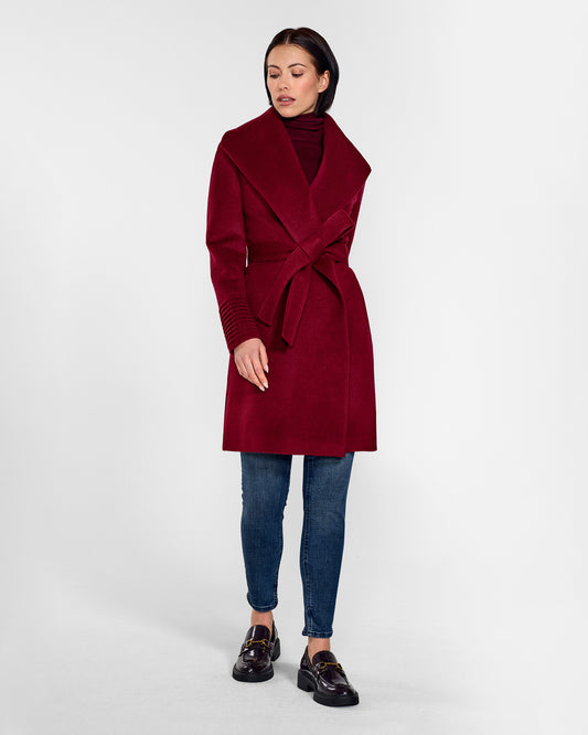 Front view of model wearing a Sentaler mid length garnet red coat made of baby alpaca wool, with a shawl collar, worn belted.