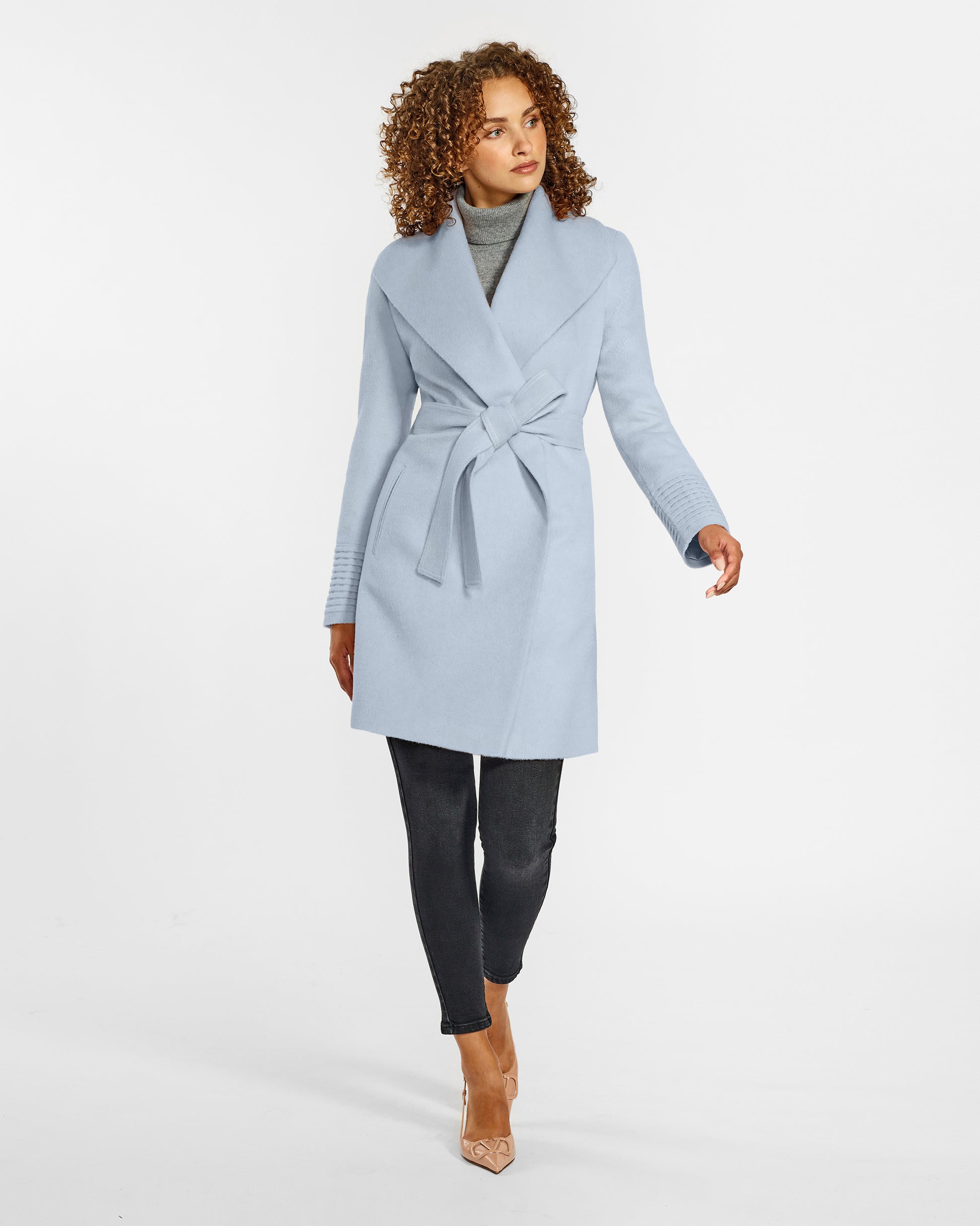 Front view of model wearing a Sentaler mid length powder blue coat made of baby alpaca wool, with a shawl collar, worn belted.
