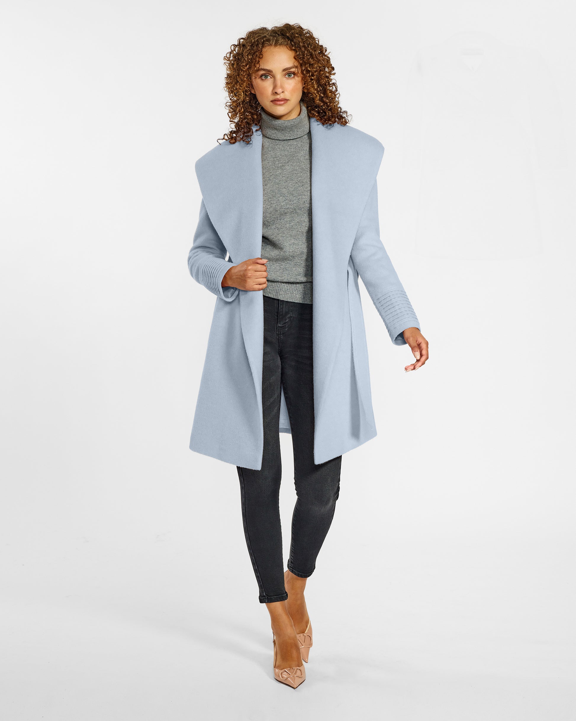 Front view of model wearing a Sentaler mid length powder blue coat made of baby alpaca wool, with a shawl collar, worn open.