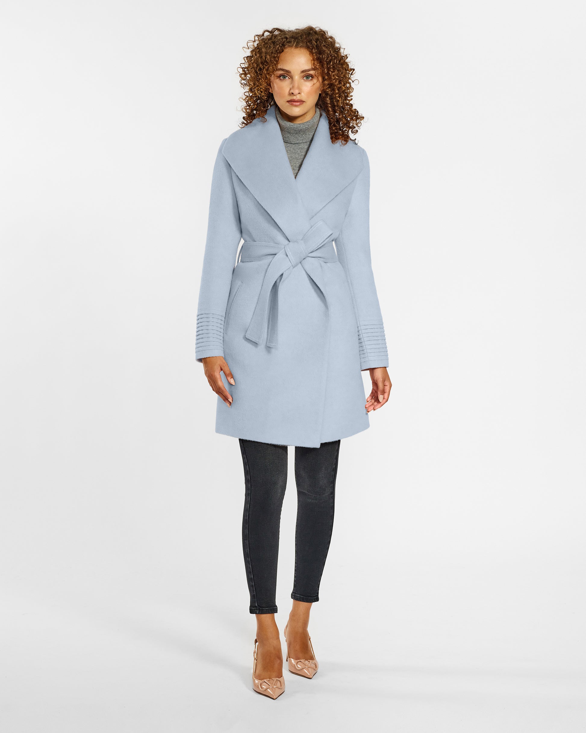 Front view of model wearing a Sentaler mid length powder blue coat made of baby alpaca wool, with a shawl collar, worn belted.