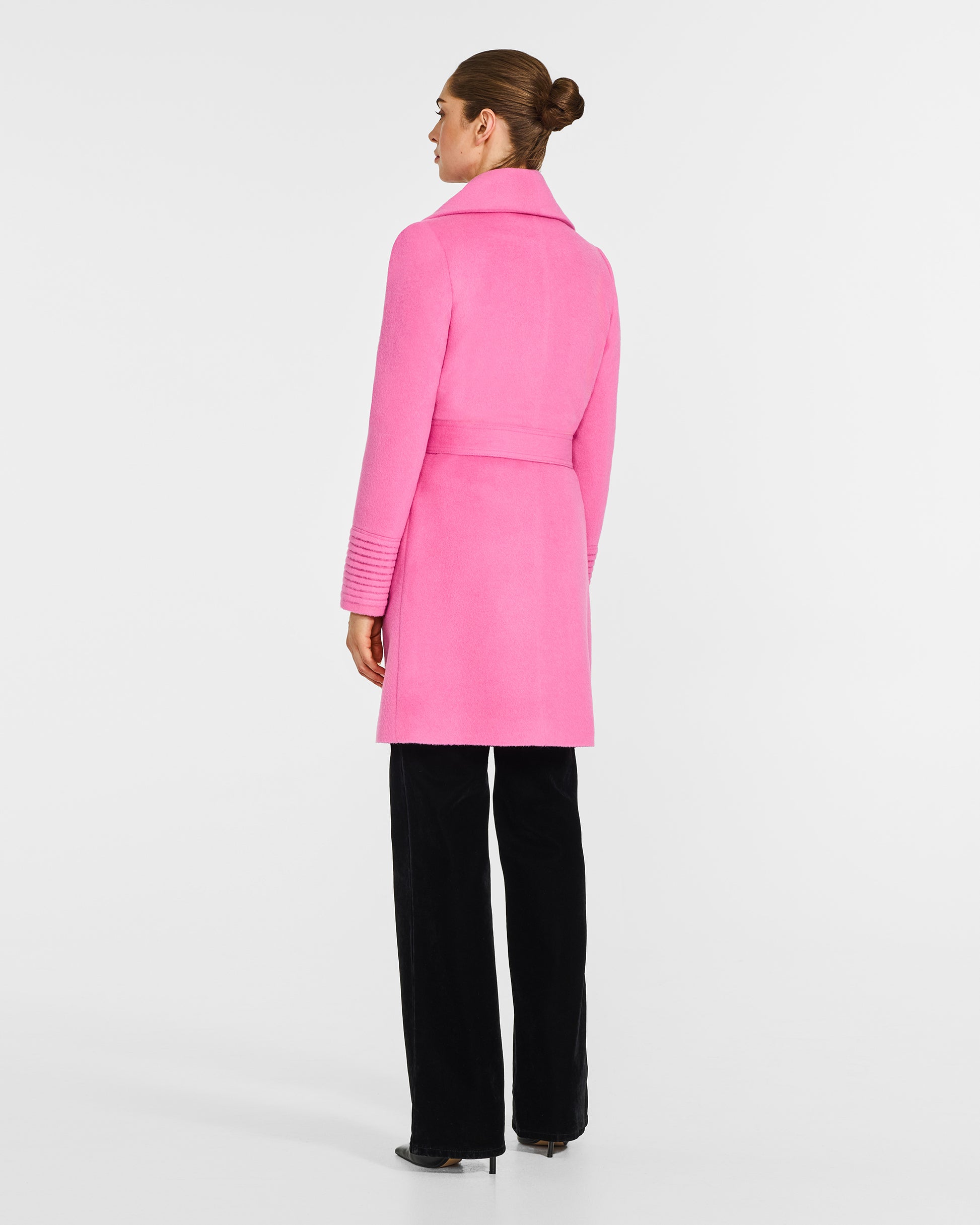 Back view of model wearing a Sentaler mid length cosmetic pink coat made of baby alpaca wool, with a shawl collar, worn belted.