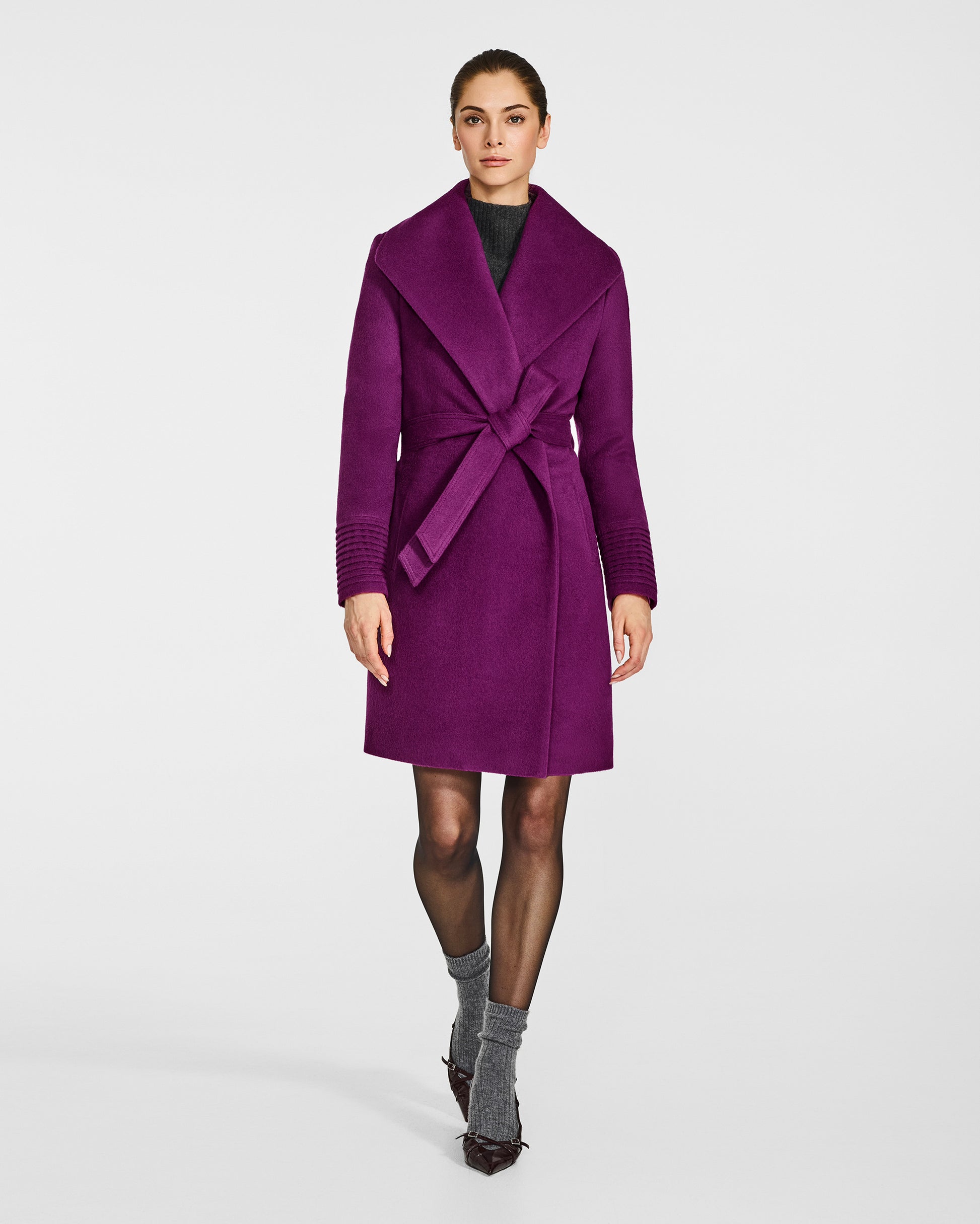 Front view of model wearing a Sentaler mid length dark mulberry purple coat made of baby alpaca wool, with a shawl collar, worn belted.