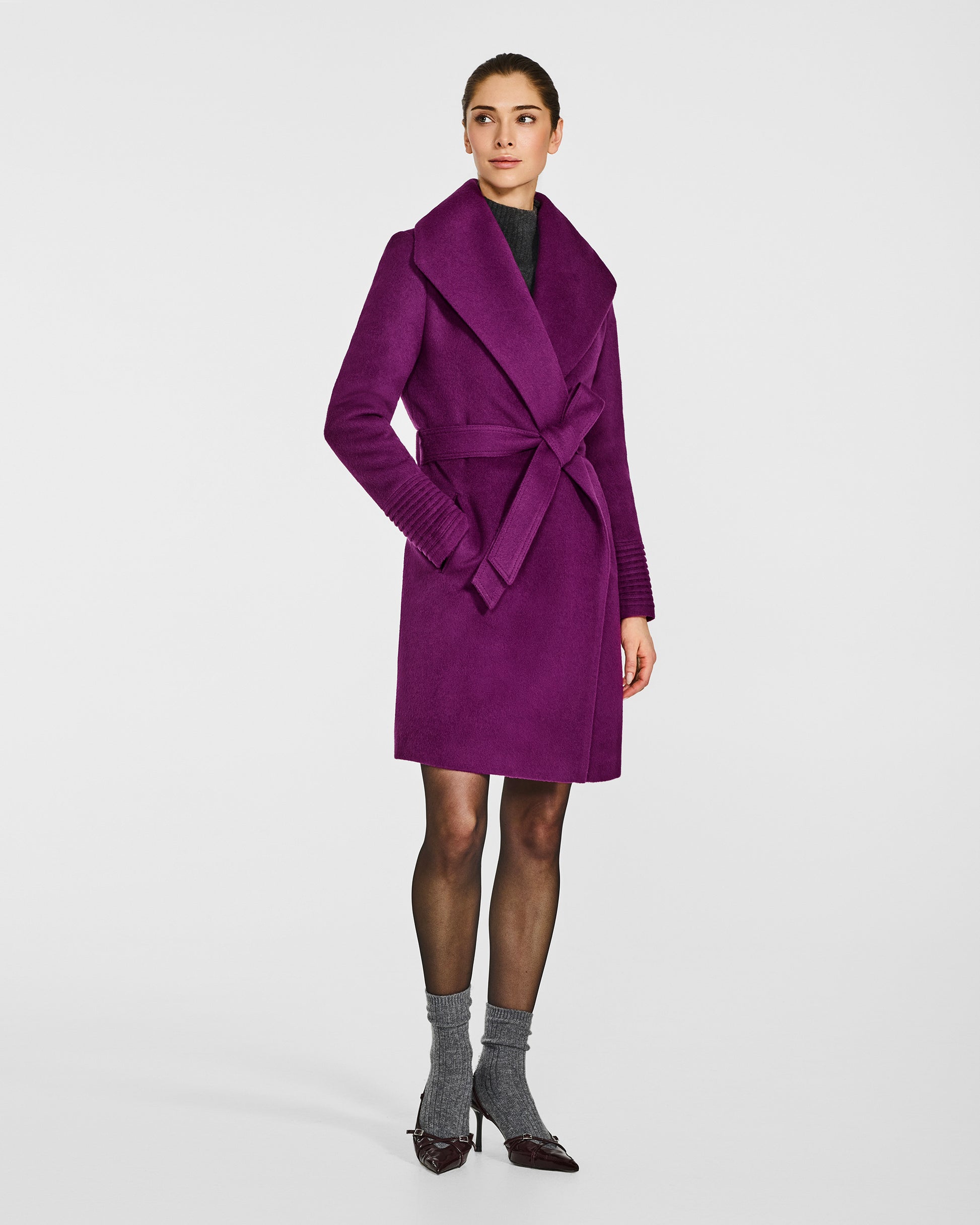 Side view of model wearing a Sentaler mid length dark mulberry purple coat made of baby alpaca wool, with a shawl collar, worn belted.