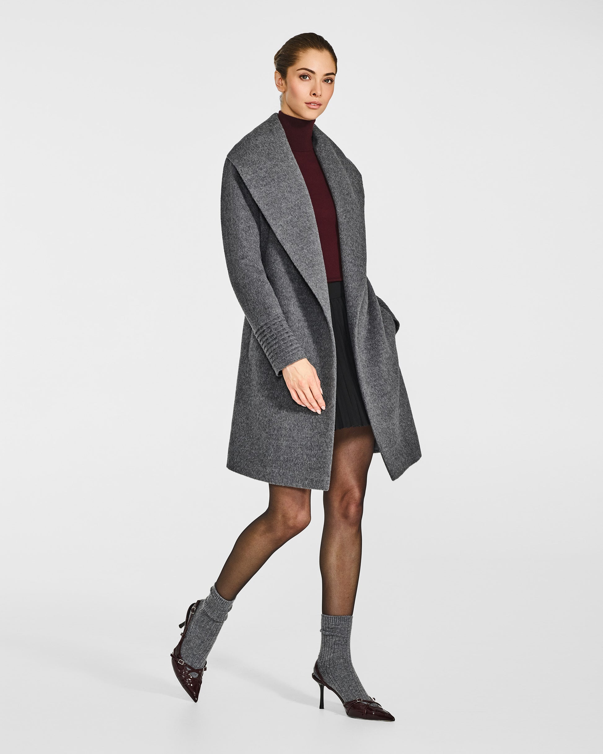 Side view of model wearing a Sentaler mid length grey mélange coat made of baby alpaca wool, with a shawl collar, worn open.