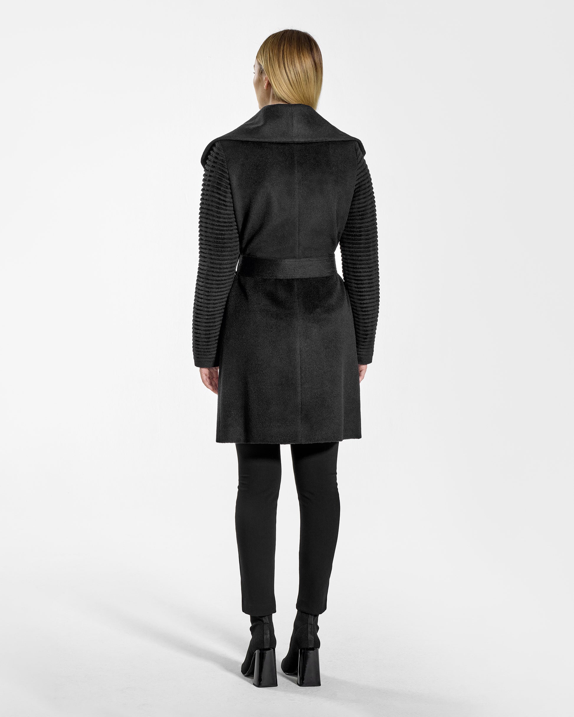 Back view of model wearing a Sentaler mid length black wrap coat made of baby alpaca wool, with ribbed sleeves, worn belted.