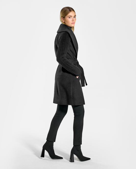 Side view of model wearing a Sentaler mid length black wrap coat made of baby alpaca wool, with ribbed sleeves, worn belted.