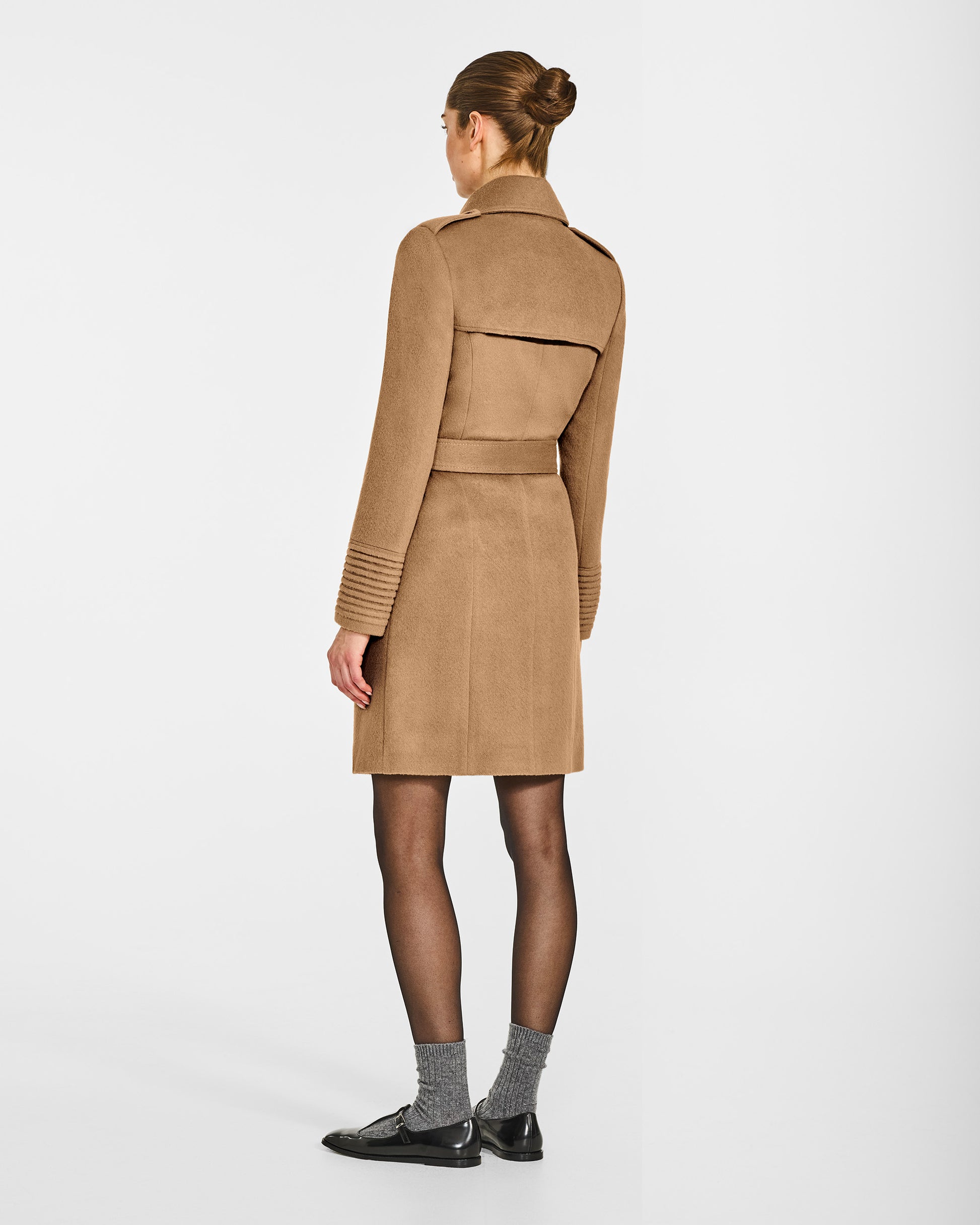 Back view of model wearing a Sentaler mid length dark camel trench coat made of baby alpaca wool, with a spread collar, worn belted.