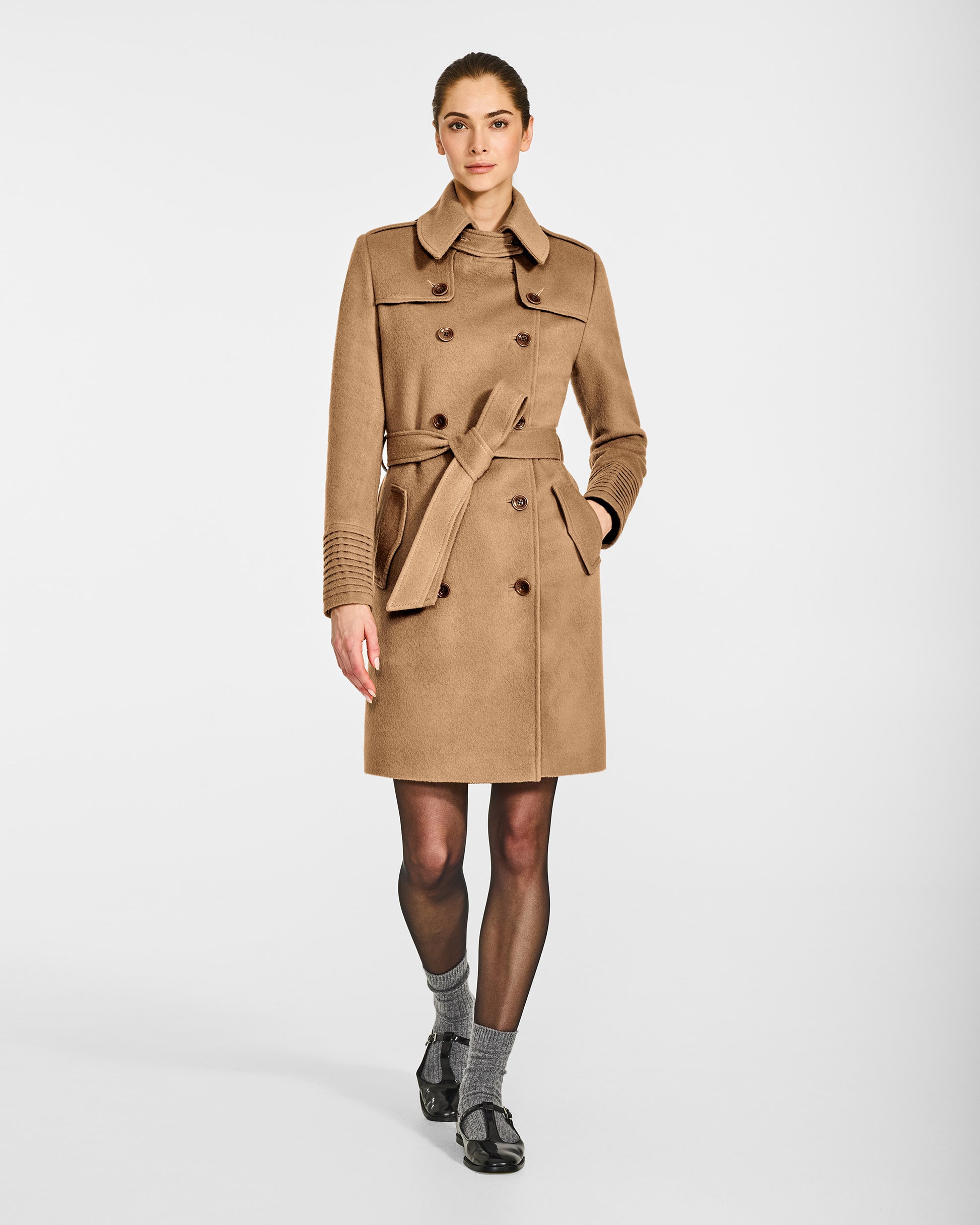 Front view of model wearing a Sentaler mid length dark camel trench coat made of baby alpaca wool, with a spread collar, worn buttoned and belted.
