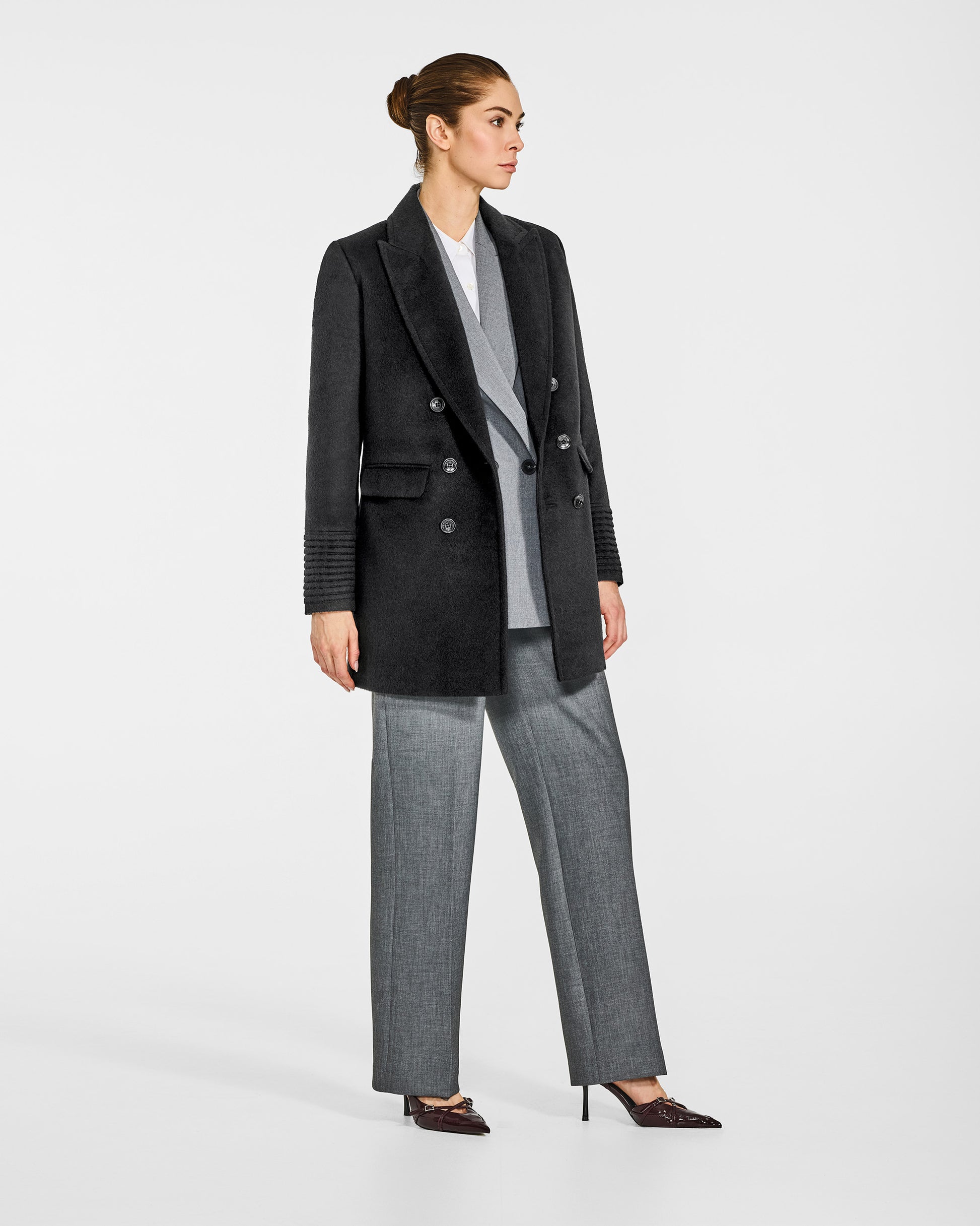 Side view of model in Sentaler black topcoat with peak collar in baby alpaca wool, open.