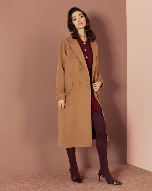 Side view of model wearing a Sentaler dark camel double breasted coat made of baby alpaca wool, with a notched collar, worn open.