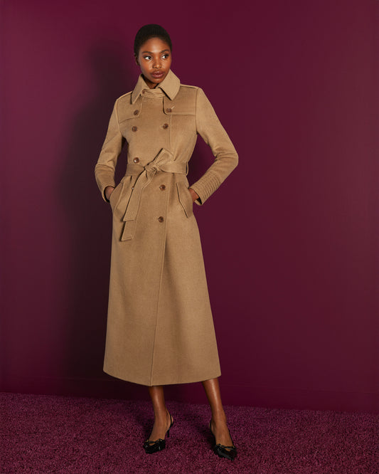 Front view of model in Sentaler maxi dark camel trench coat made of baby alpaca wool, with a spread collar, worn buttoned & belted.