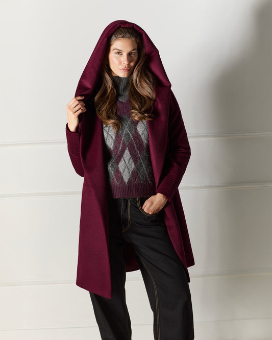 Front view of model wearing a Sentaler mid length cherry lacquer coat made of baby alpaca wool, with a hooded collar, worn open.