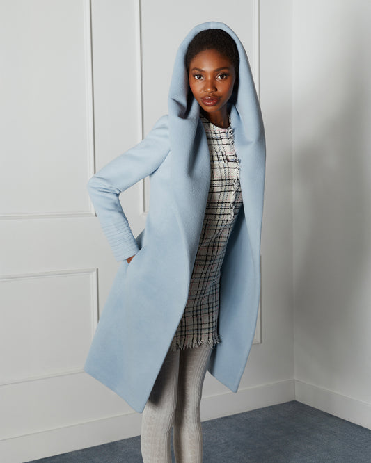 Side view of model wearing a Sentaler mid length glacial blue coat made of baby alpaca wool, with a hooded collar, worn open.