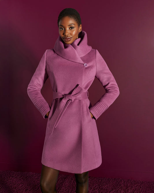 Front view of model wearing a Sentaler mid length mauve pink coat made of baby alpaca wool, with a hooded collar, worn belted.